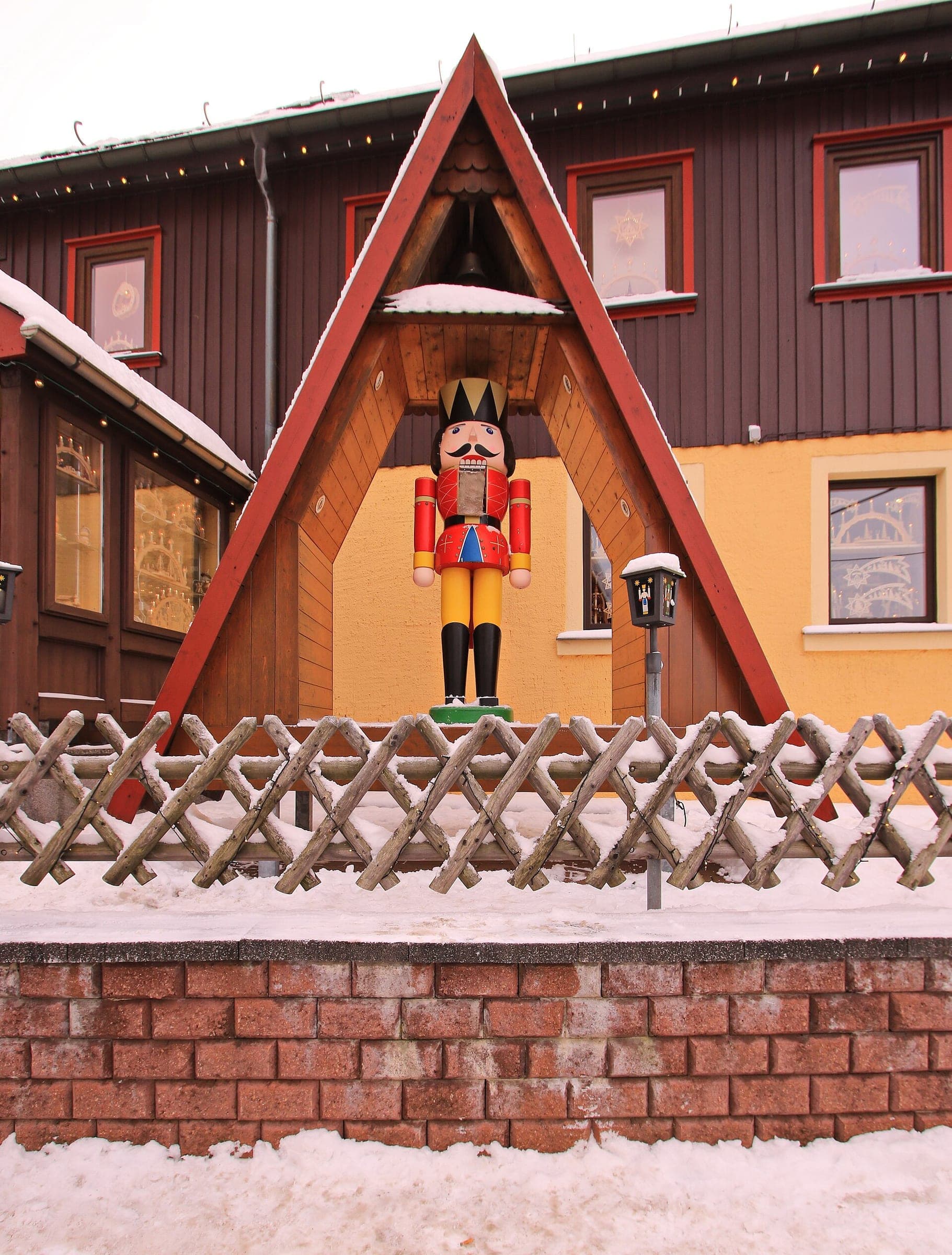 A giant painted nutcracker stands under a red wooden gable above a snowy fence in Seiffen.