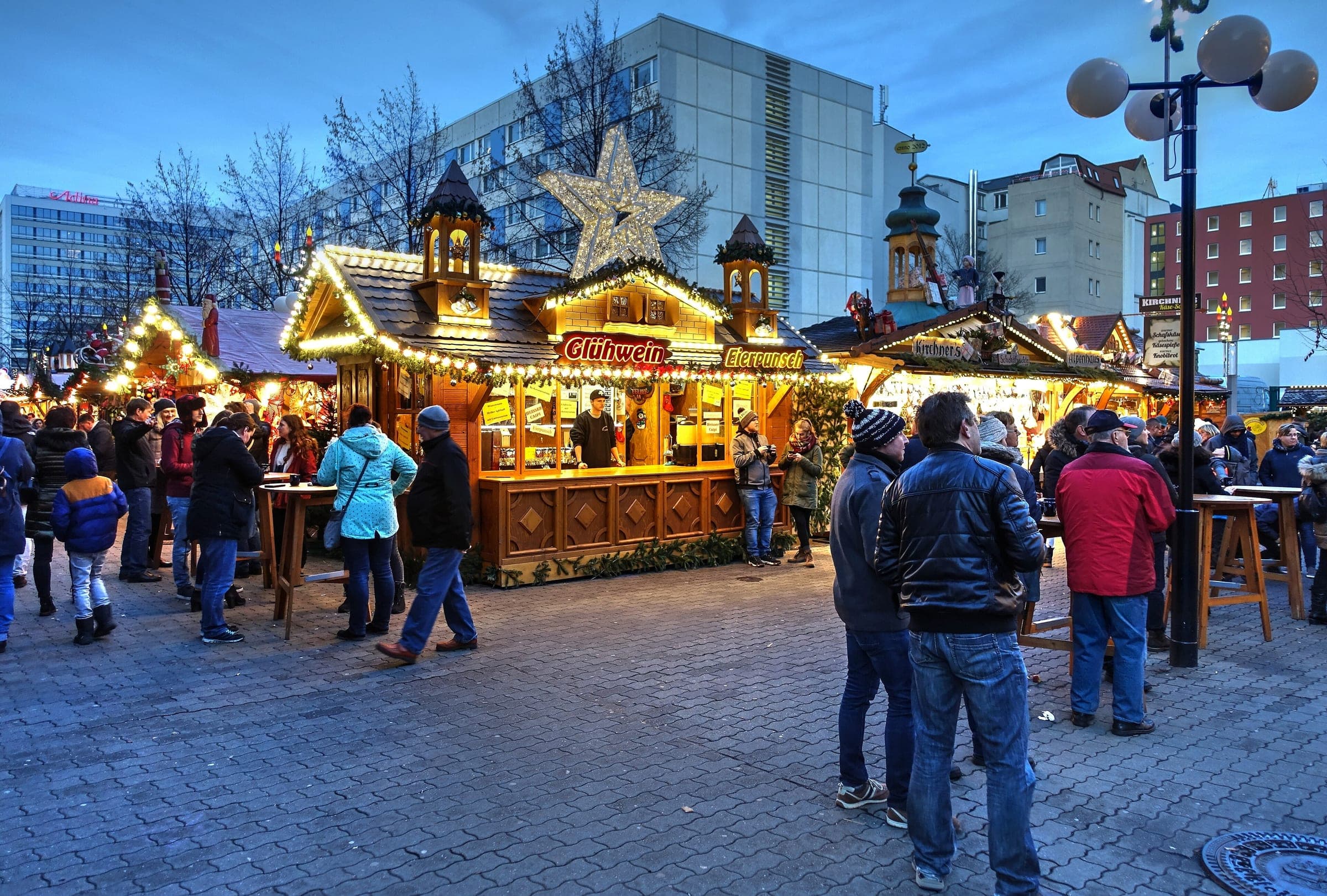 Drinkers gather at a lit Glühwein stand on Reichsstraße at Leipzig's Christmas market at dusk