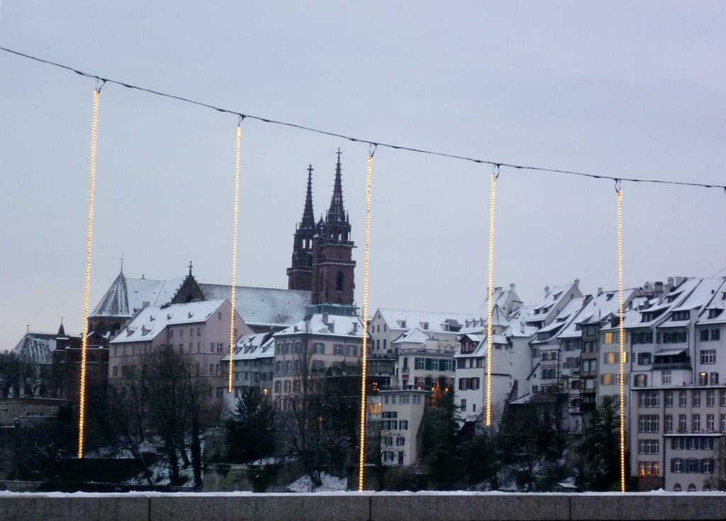 Strands of Christmas lights hang from the Mittlere Brücke in Basel in front of the snowy Minster and Rhine houses