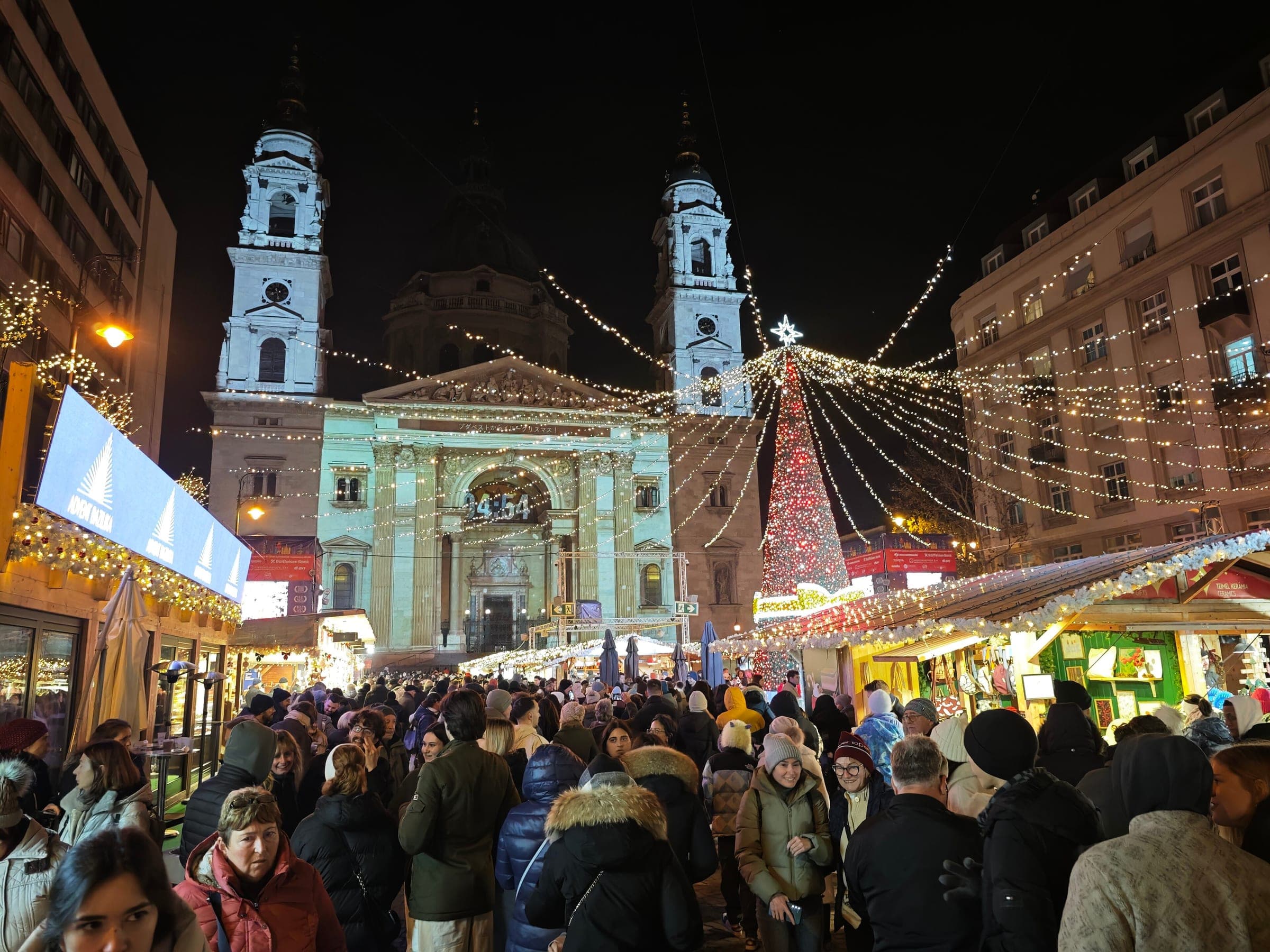 Crowds fill Szent István tér under strings of lights as the projection plays on the basilica front in Budapest.