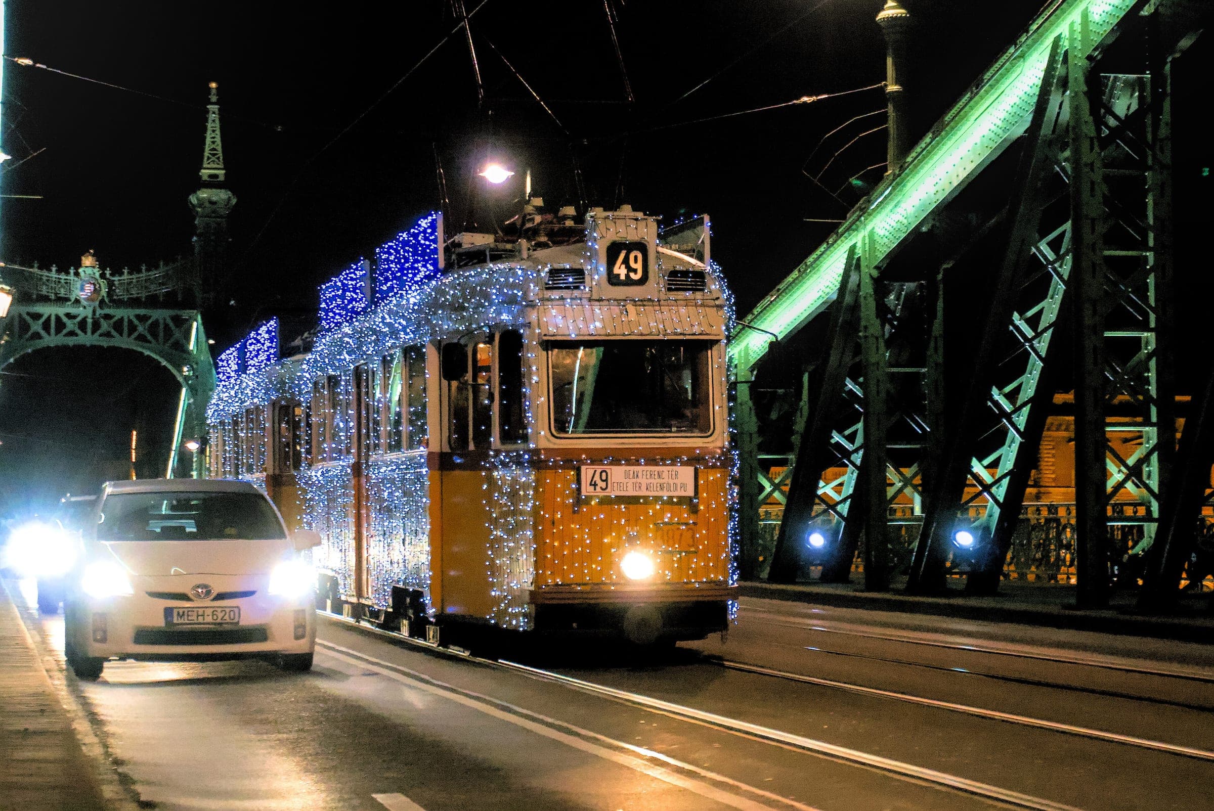 The Light Tram crosses Budapest's green-lit Liberty Bridge on line 49, its body covered in fairy lights.