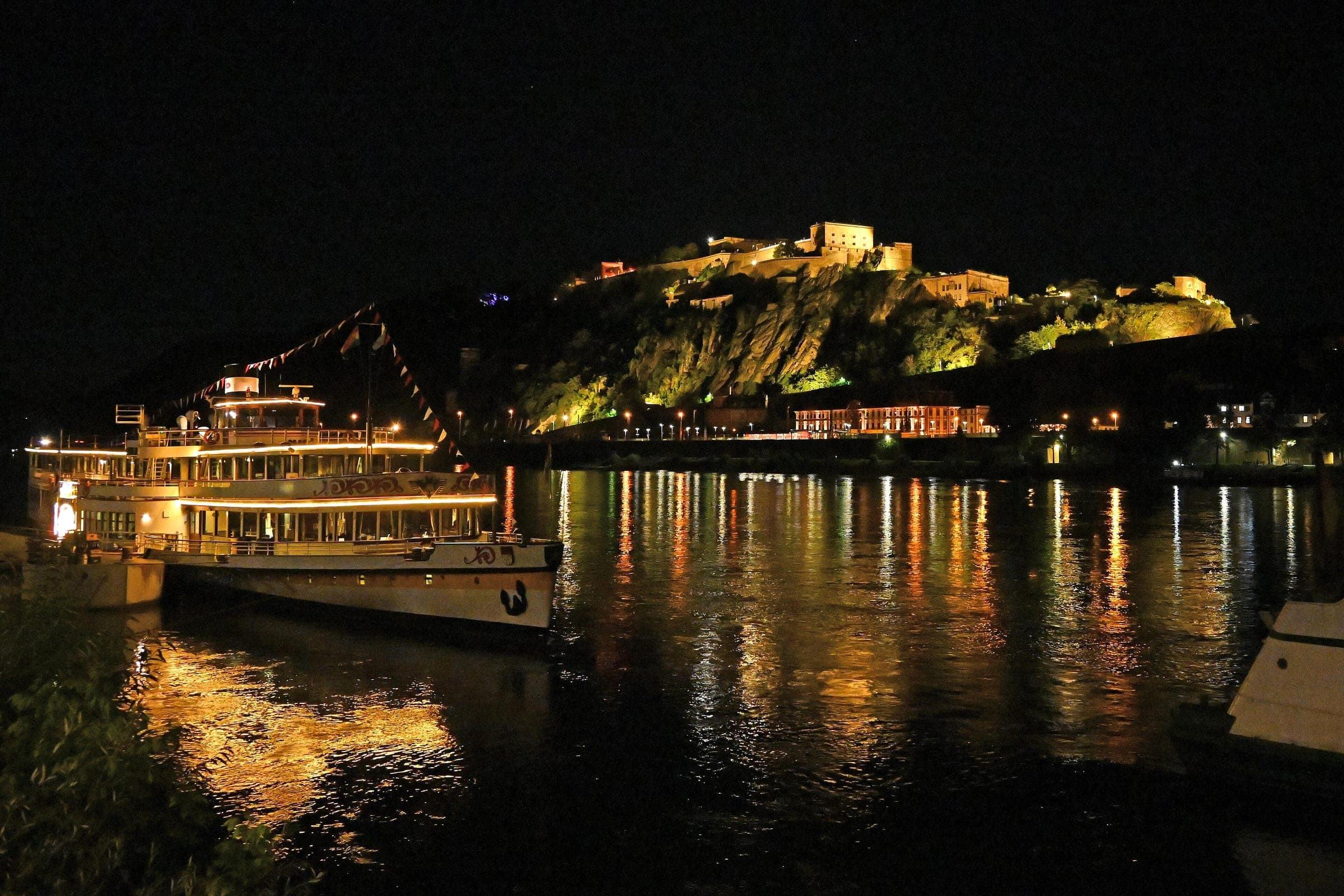 Ehrenbreitstein Fortress glows on its rock above the Rhine and a moored paddle steamer at night