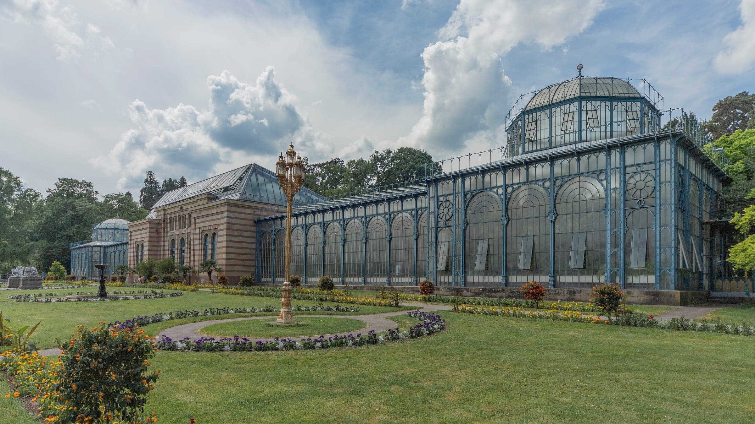 Lawns and flower beds spread in front of the Moorish glasshouses of the Wilhelma in Stuttgart on a summer day.