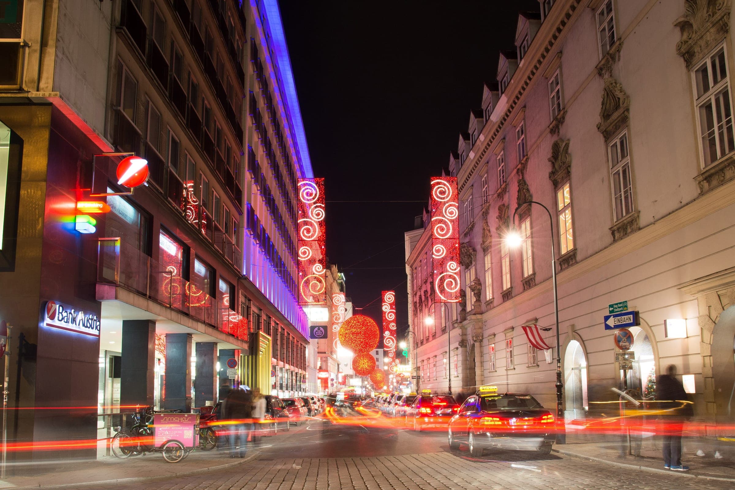 Red spiral banners and glowing globes light the Rotenturmstrasse in Vienna at night as traffic streaks past.