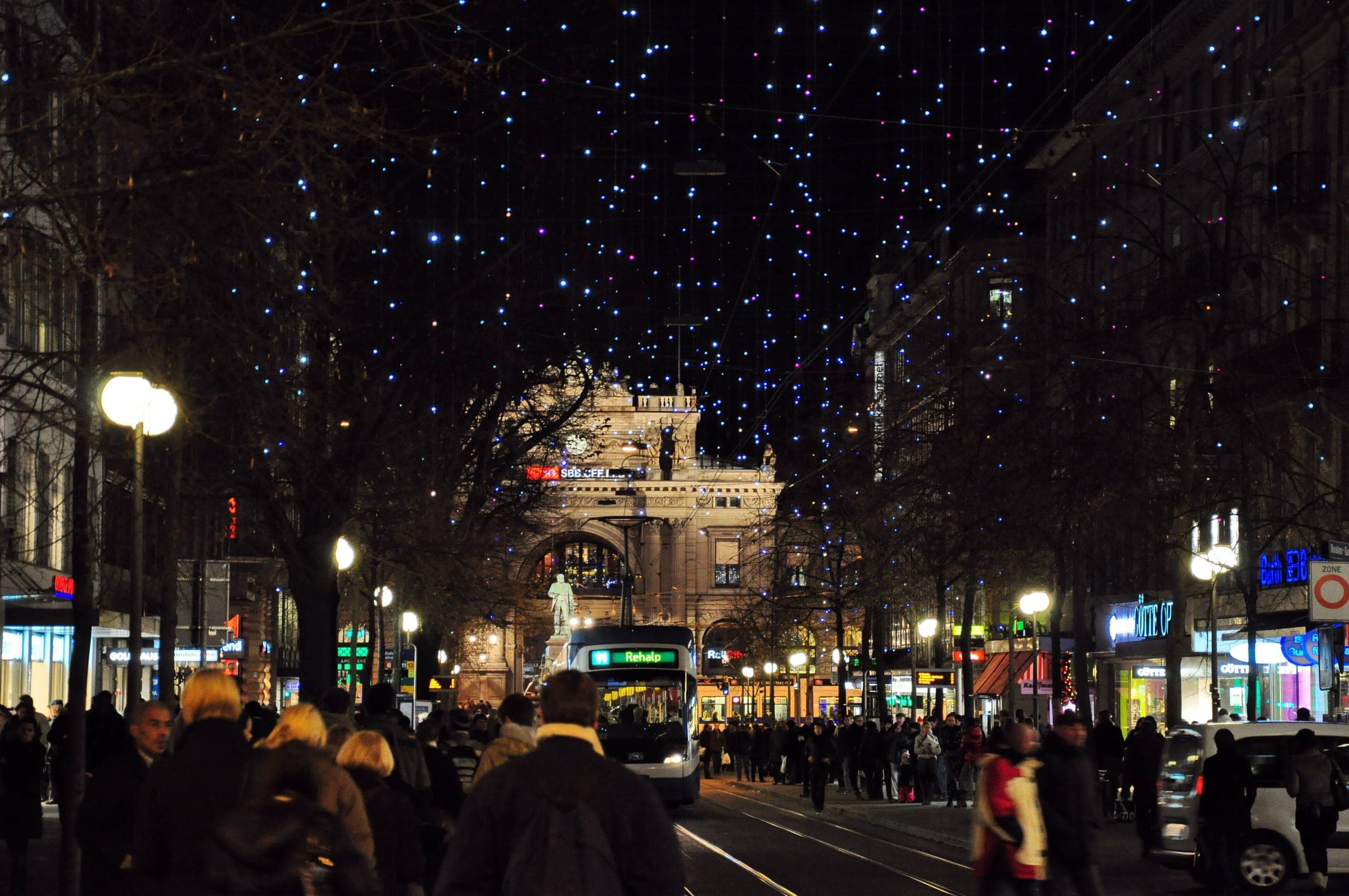 Shoppers crowd Bahnhofstrasse in Zurich under the Christmas lights with the main station at the far end