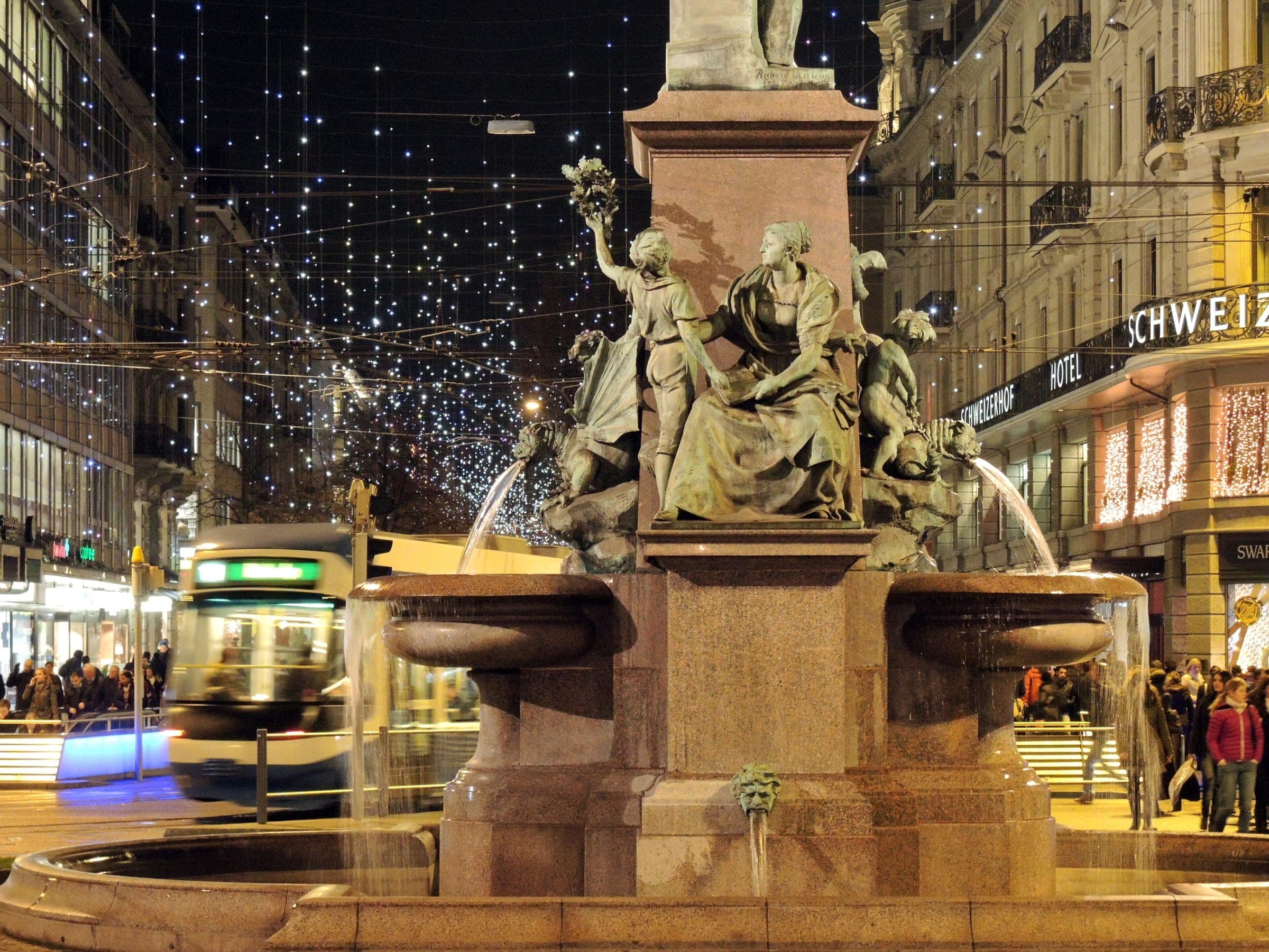 Christmas lights hang over Bahnhofstrasse in Zurich behind the Alfred Escher fountain and a passing tram