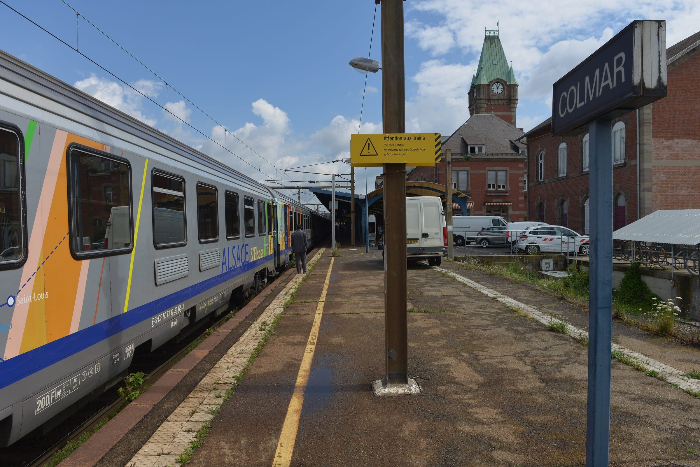 A TER Alsace train waits at a Colmar station platform below the station's clock tower.
