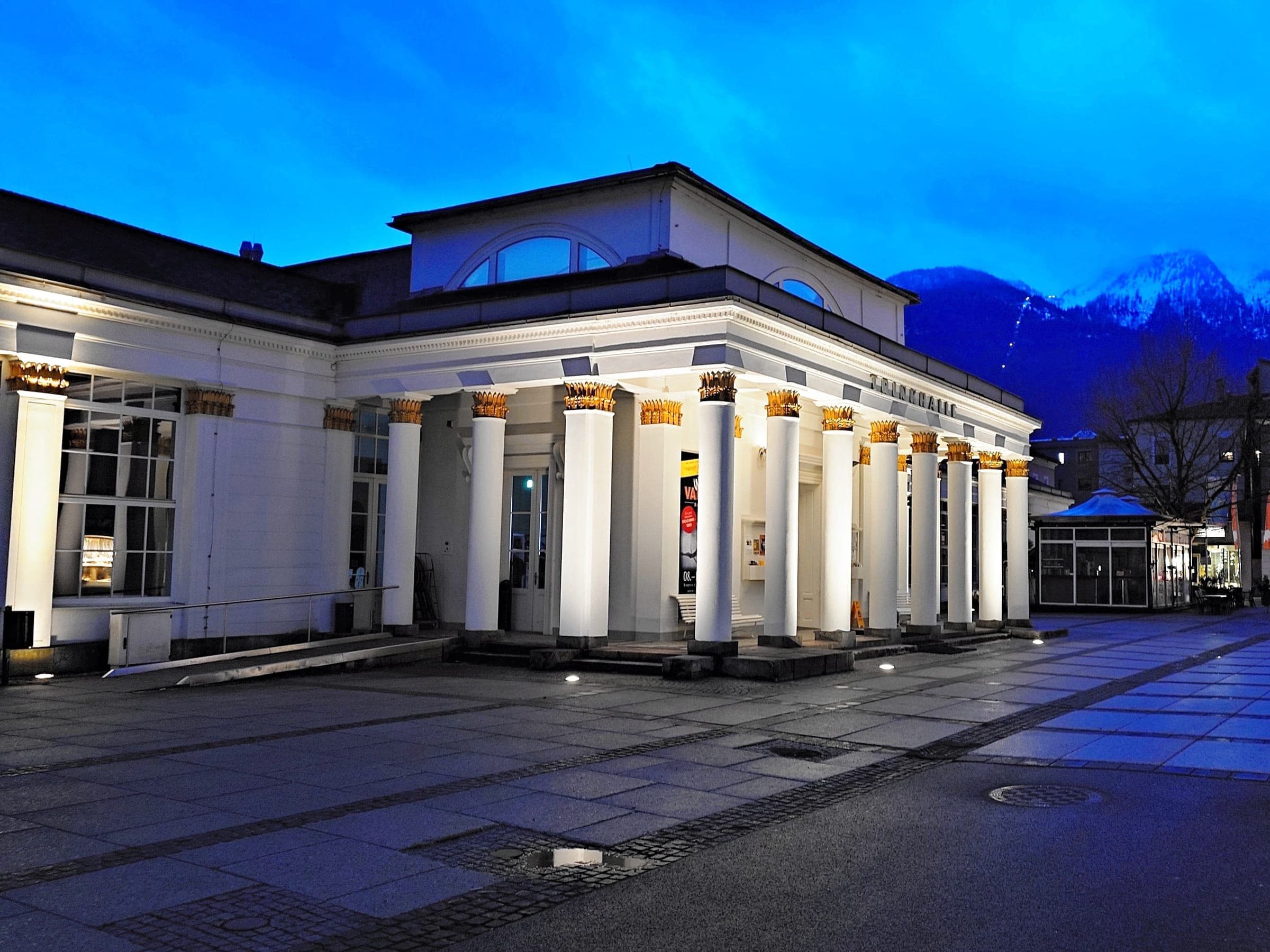The Trinkhalle in Bad Ischl glows under a blue-hour sky with snow on the peaks behind