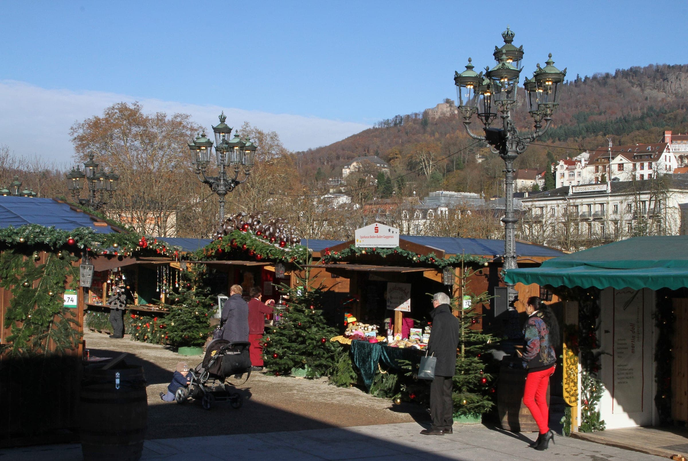 Market stalls stand under the old lamps by the Kurhaus colonnade in Baden-Baden with the hills behind.