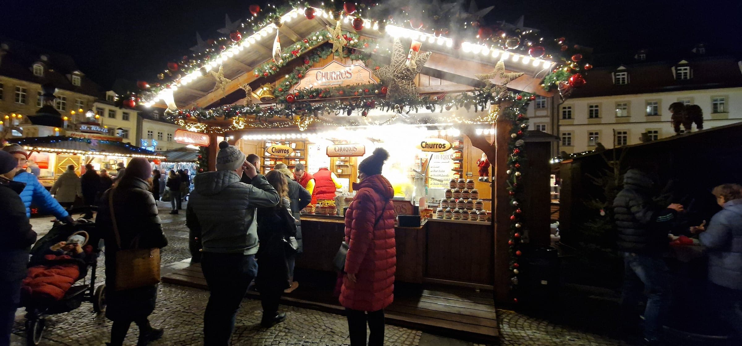 Visitors queue at a garlanded churros stall at the Bamberg Christmas market in the evening
