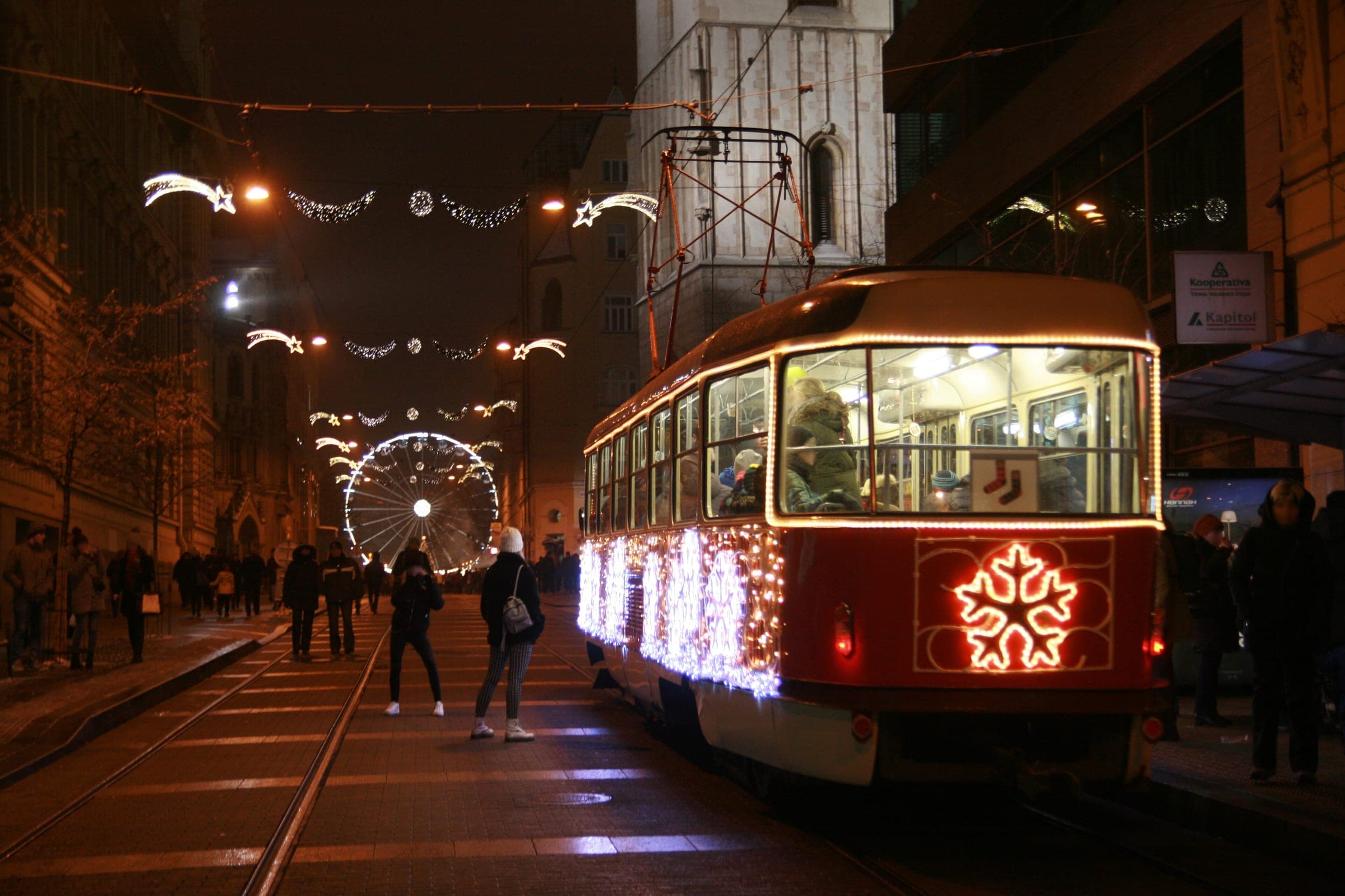 Brno's Christmas tram glows with fairy lights as it runs past the market toward náměstí Svobody.