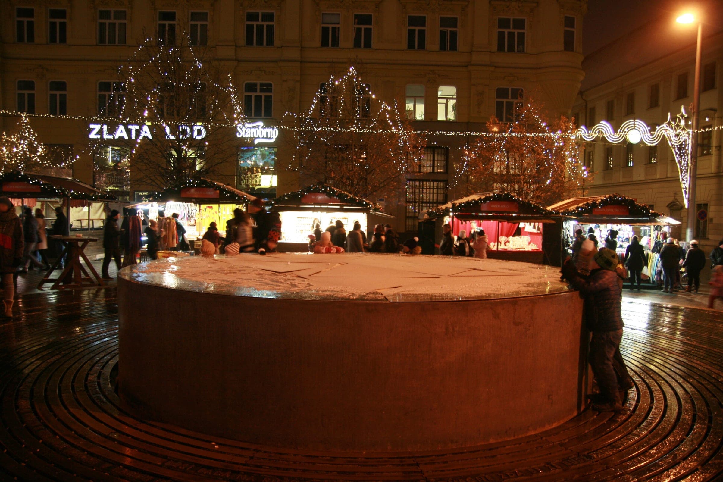 Lit wooden stalls ring the boarded-over fountain on náměstí Svobody during Brno's Christmas market.