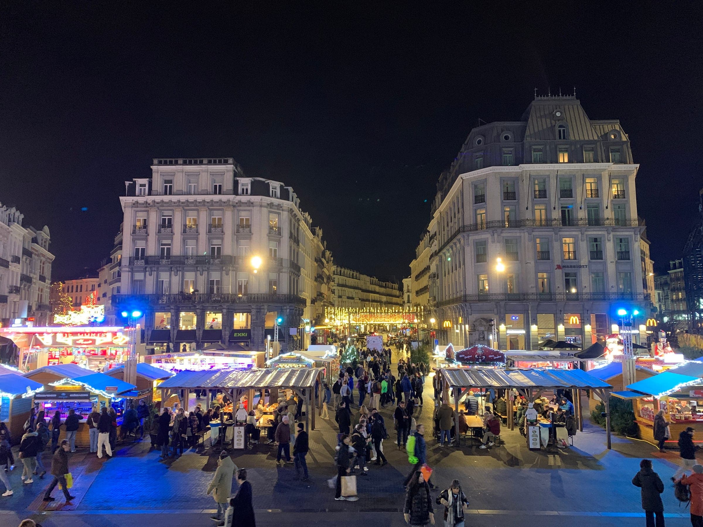 Crowds walk between lit Winter Wonders chalets near the Bourse in Brussels on a December night.