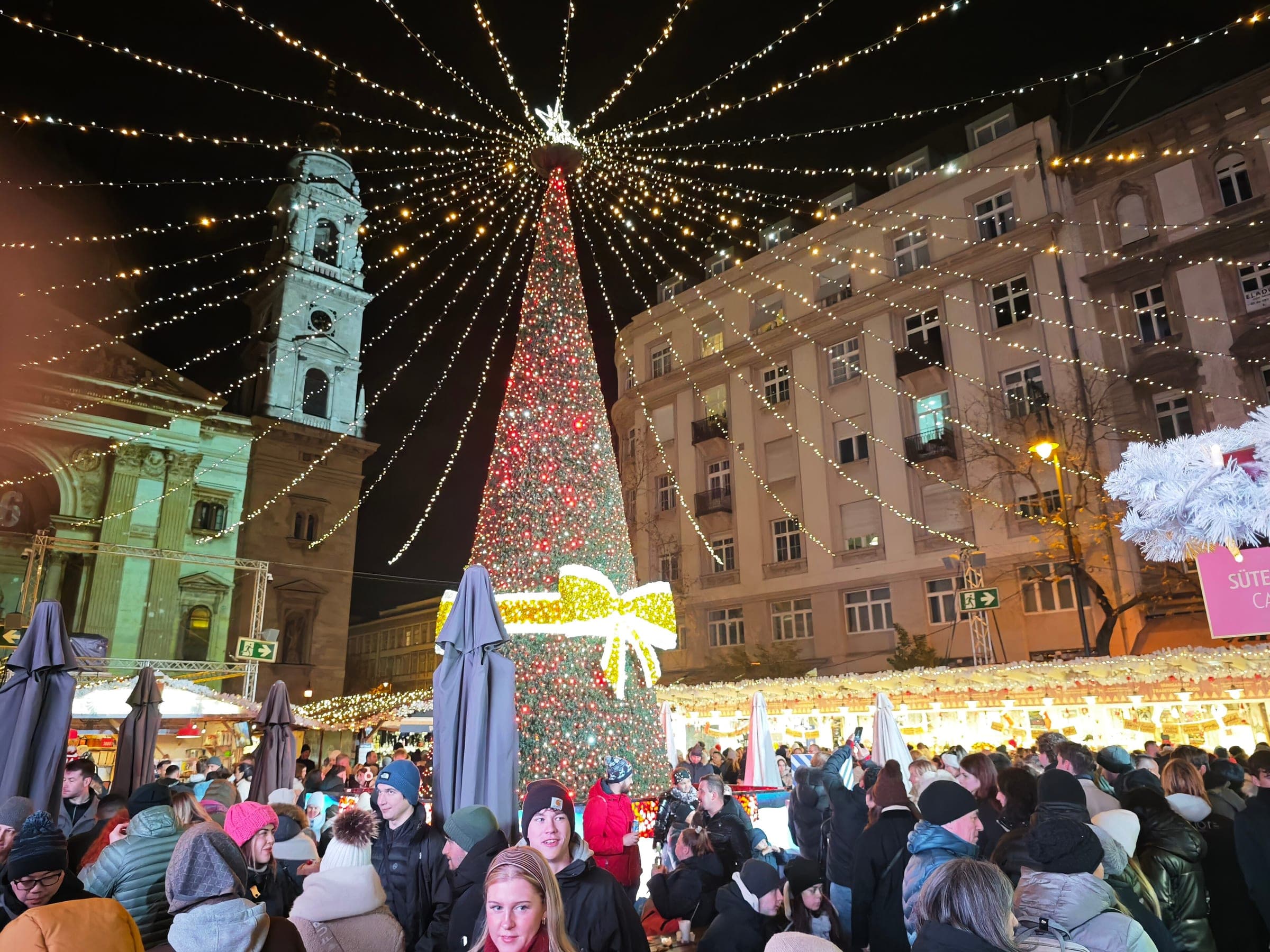 A tall tree of red lights and a gold bow stands beside a basilica tower at the Budapest Advent market.