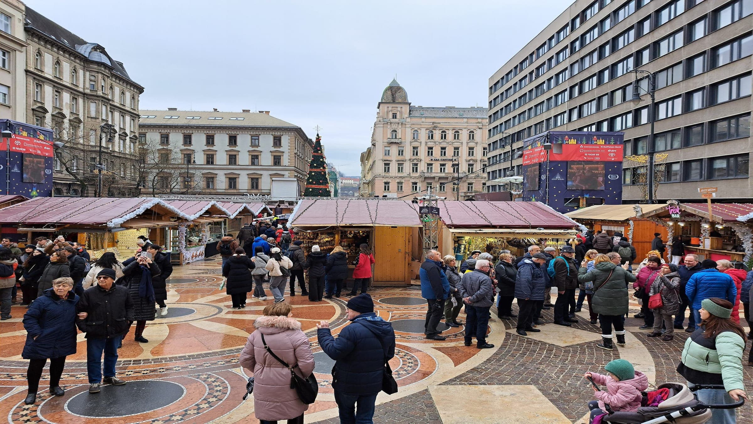 Visitors cross the patterned paving of Szent István tér between the wooden stalls of the Budapest Advent market.