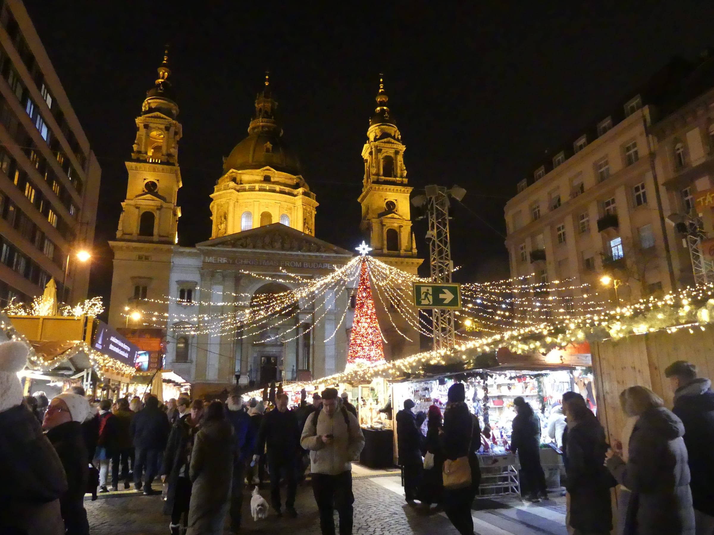 The floodlit towers and dome of St. Stephen's Basilica rise over the lit stalls of Advent Bazilika in Budapest.