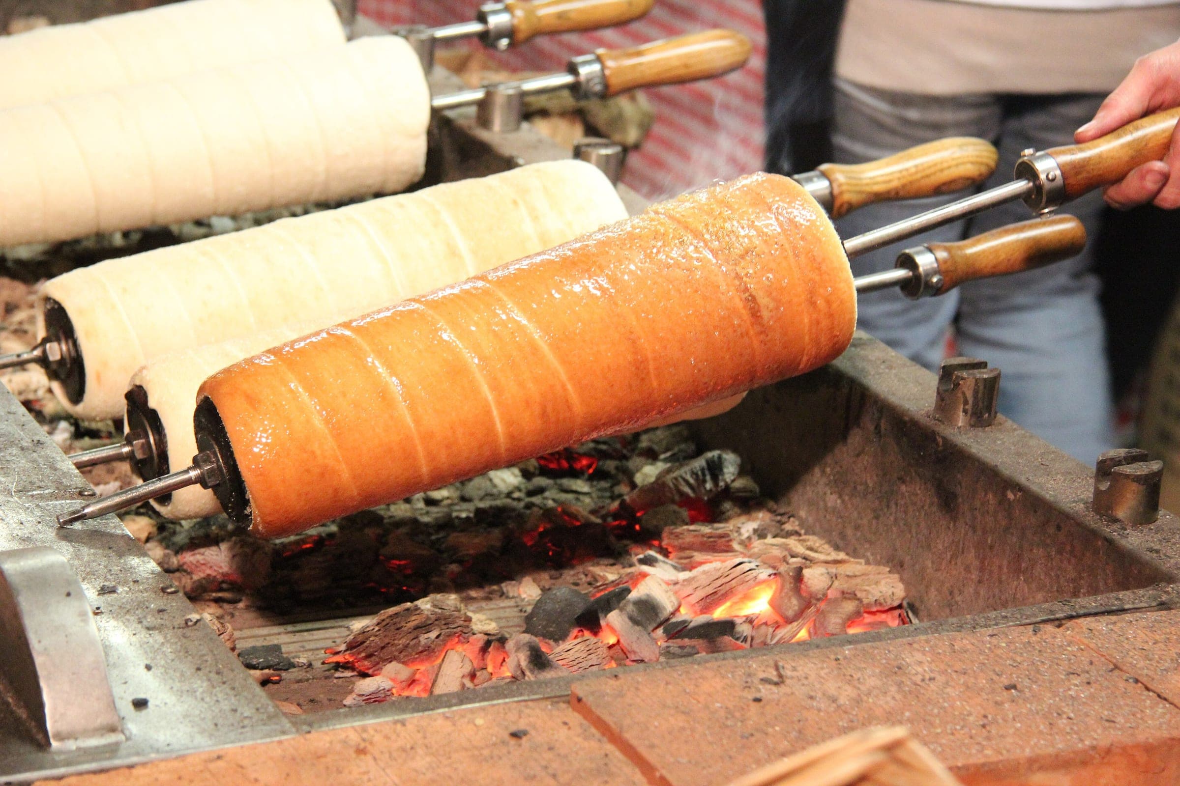 Chimney cakes turn on wooden spits over glowing coals at the Vörösmarty tér Christmas market in Budapest.