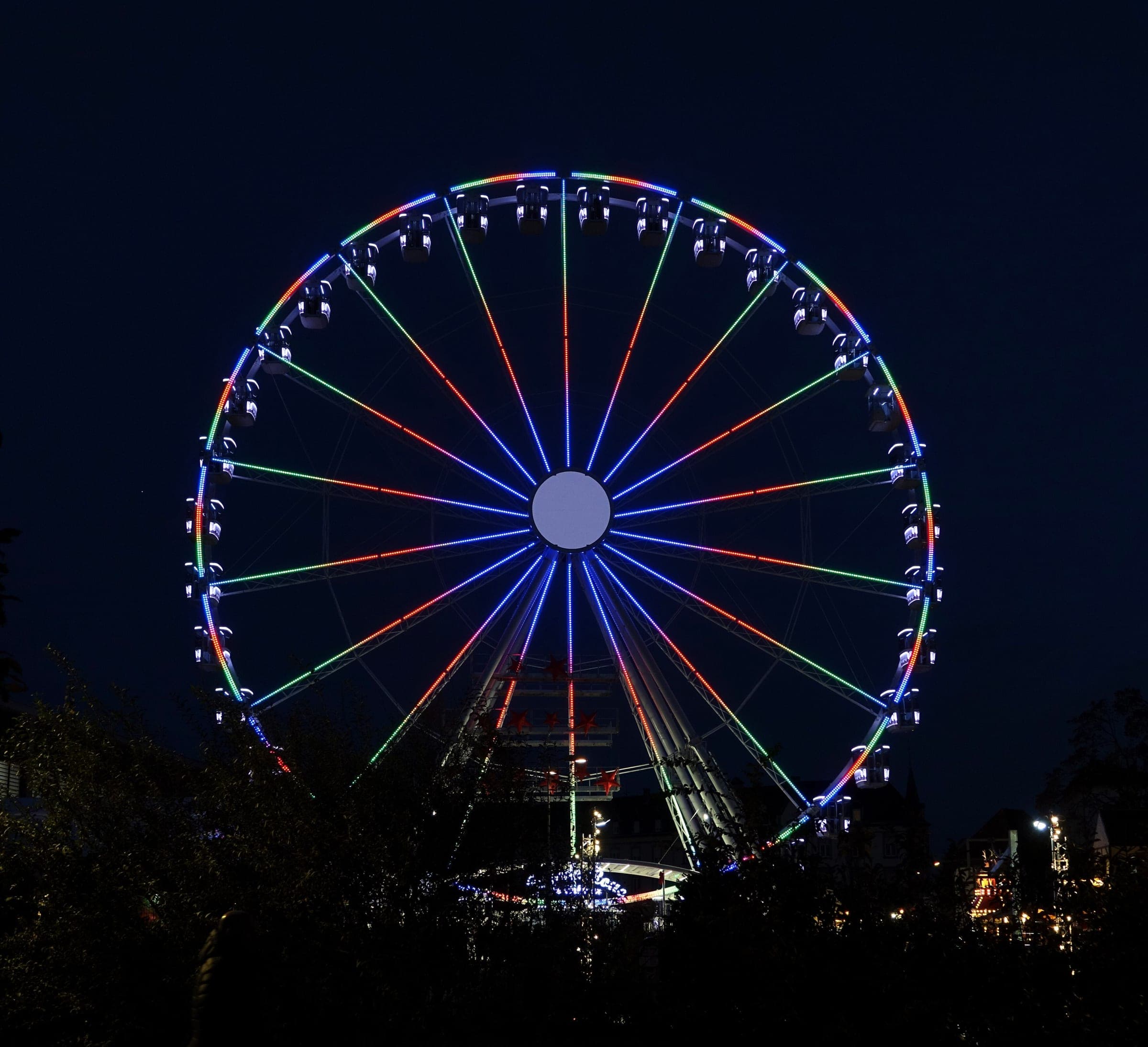 Coloured lights trace the spokes of the Ferris wheel at Colmar's gourmet market on rue de la Montagne Verte.