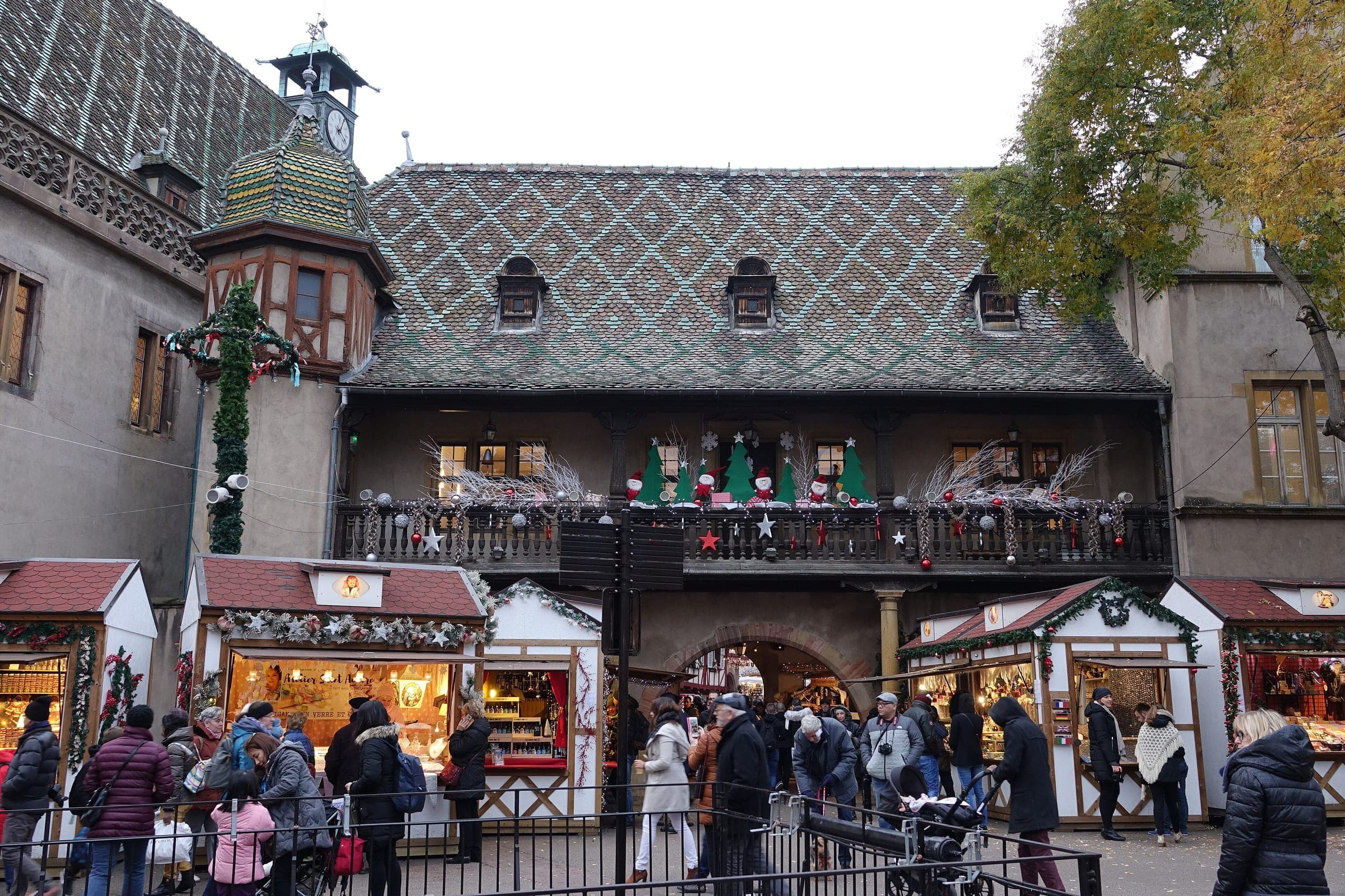 White chalets line up below the glazed tile roof and wooden gallery of the Koïfhus in Colmar.