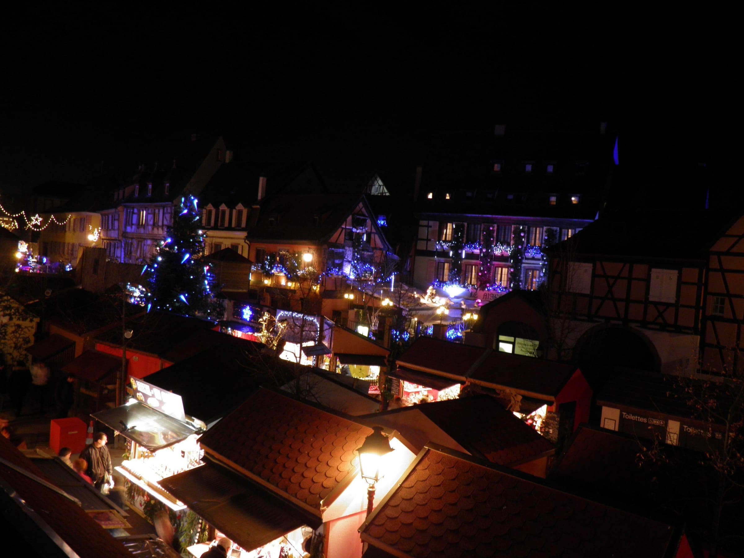 Chalet roofs and a lit tree crowd Place des Six Montagnes Noires in Colmar's Petite Venise after dark.