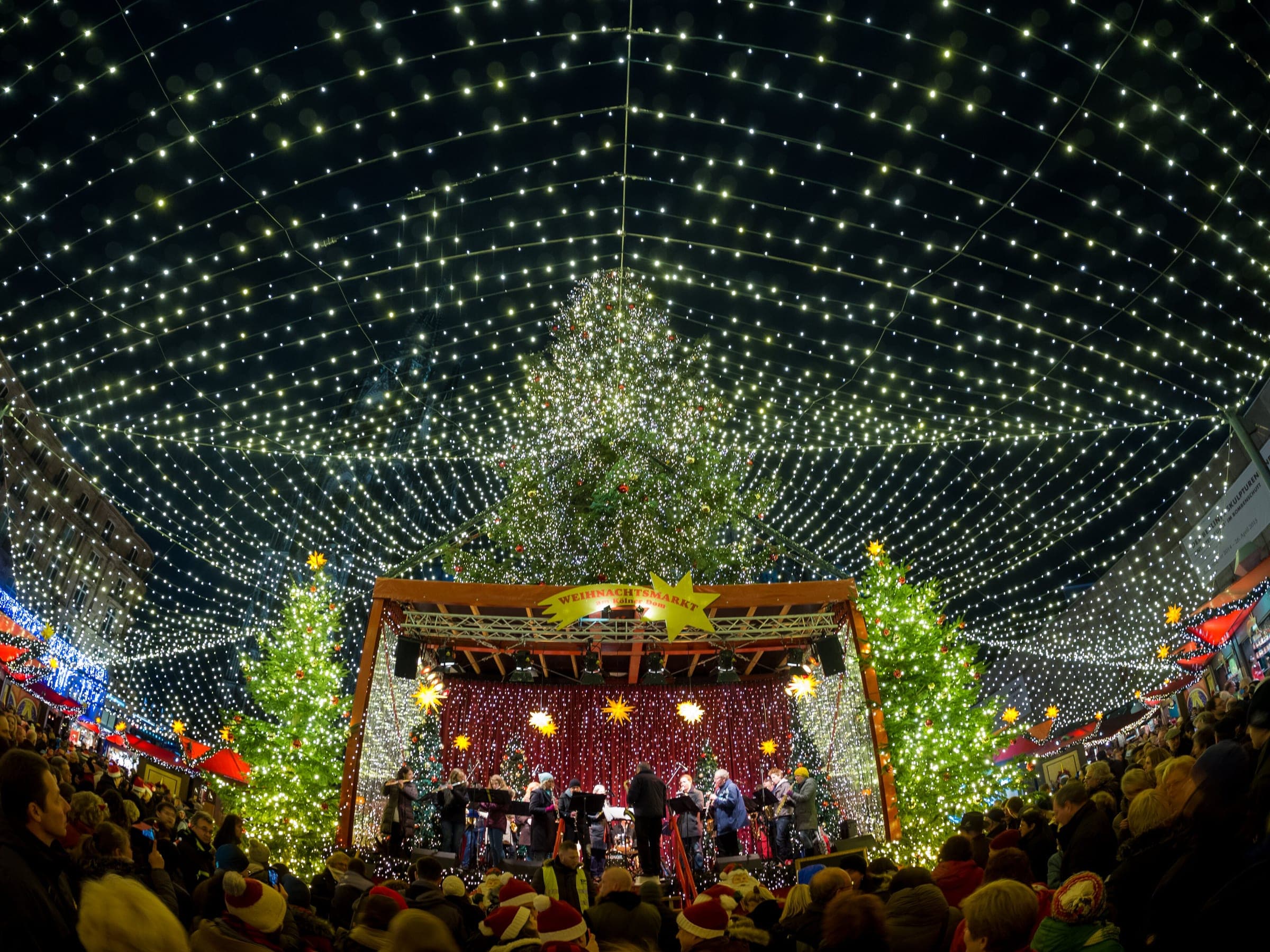 Musicians play on the stage under the canopy of lights at the Cologne Cathedral Christmas market