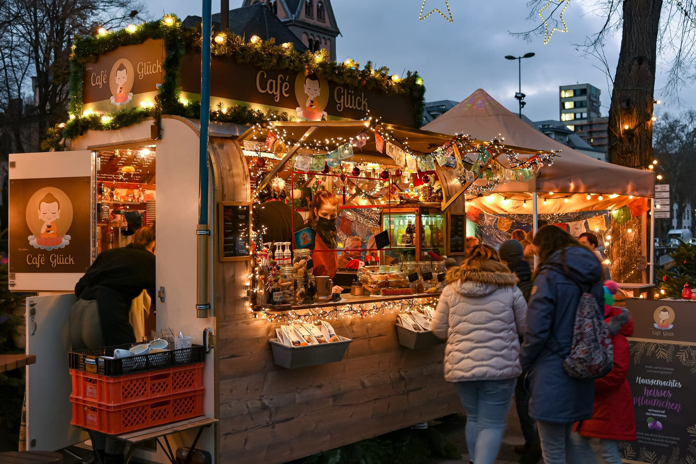 A café stall strung with lights serves visitors at the Cologne harbour Christmas market at dusk