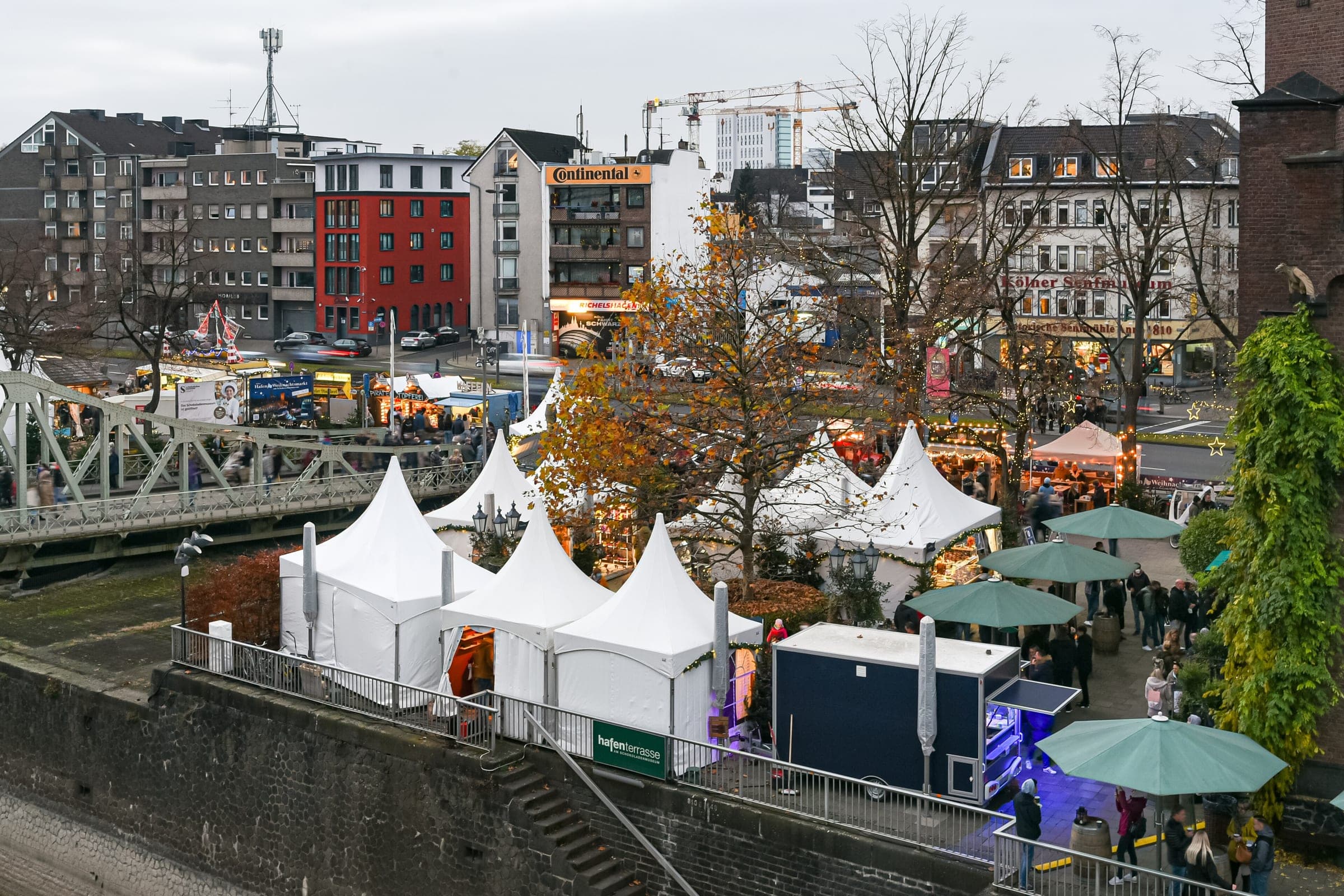 Peaked white tents of the Cologne harbour market line the Rheinauhafen quay below the swing bridge