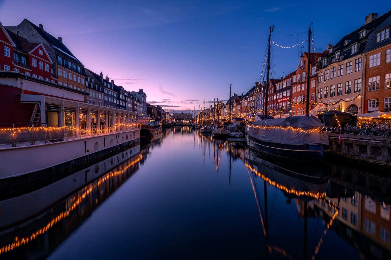 Strings of lights trace the boats and quays of Nyhavn in Copenhagen under a violet December sky.