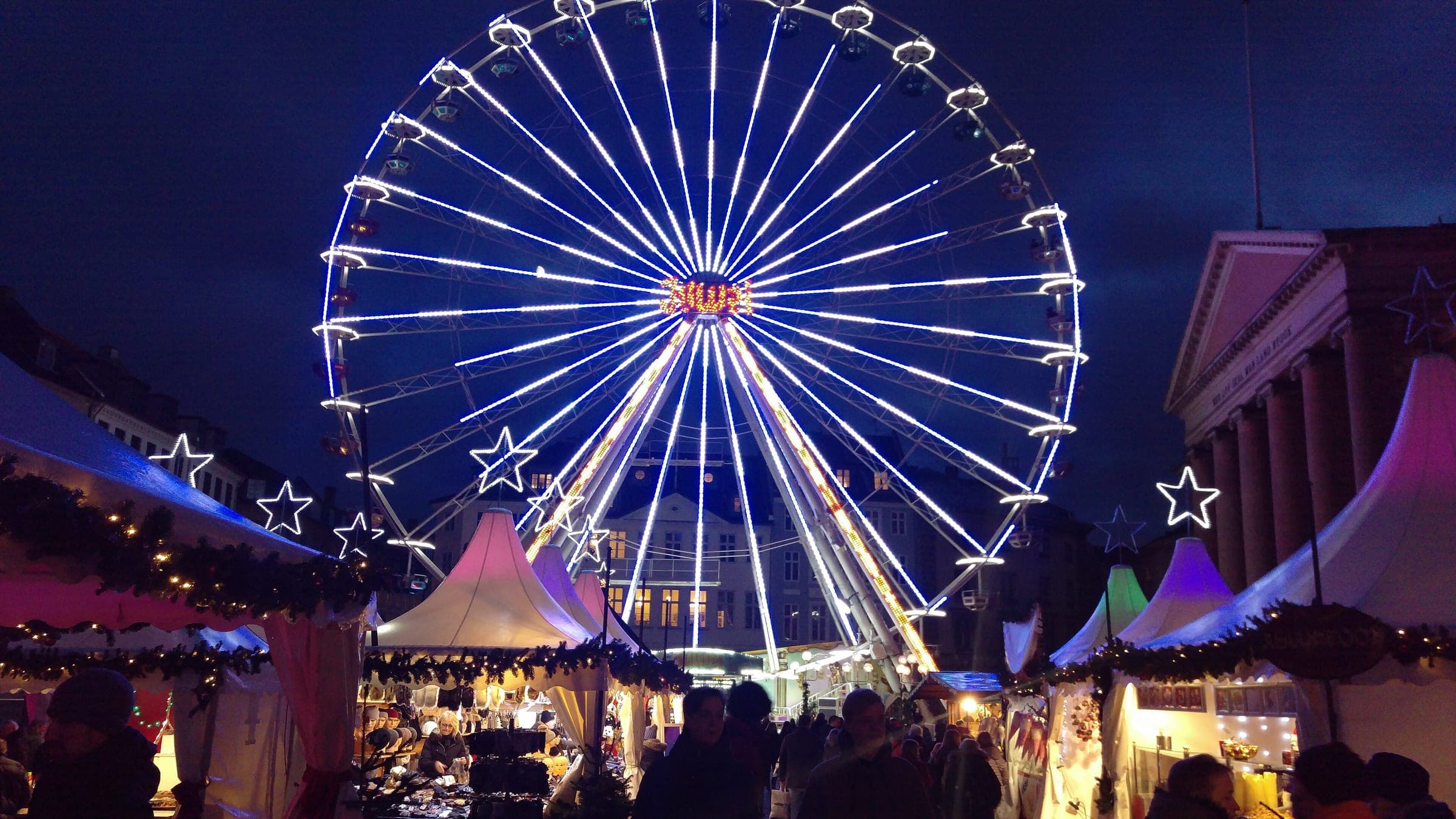A lit Ferris wheel turns above the tented stalls of the Nytorv Christmas market in Copenhagen by the courthouse.