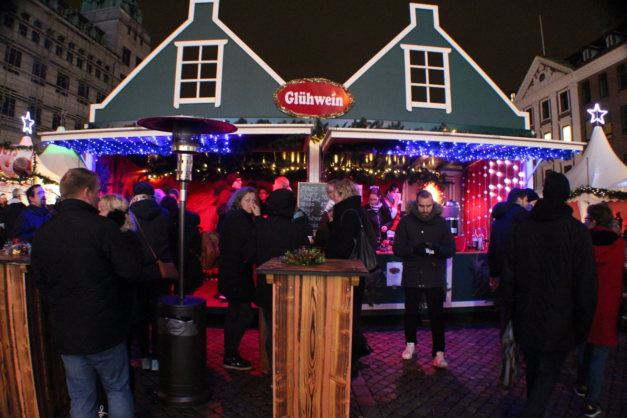 Visitors drink at standing tables outside a gabled mulled wine chalet at the Nytorv Christmas market in Copenhagen.