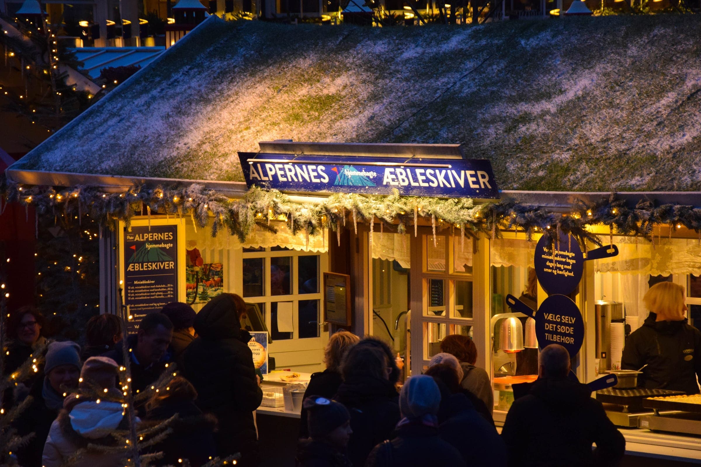 People queue at a moss-roofed æbleskiver stall at Christmas in Tivoli in Copenhagen as the light fades.