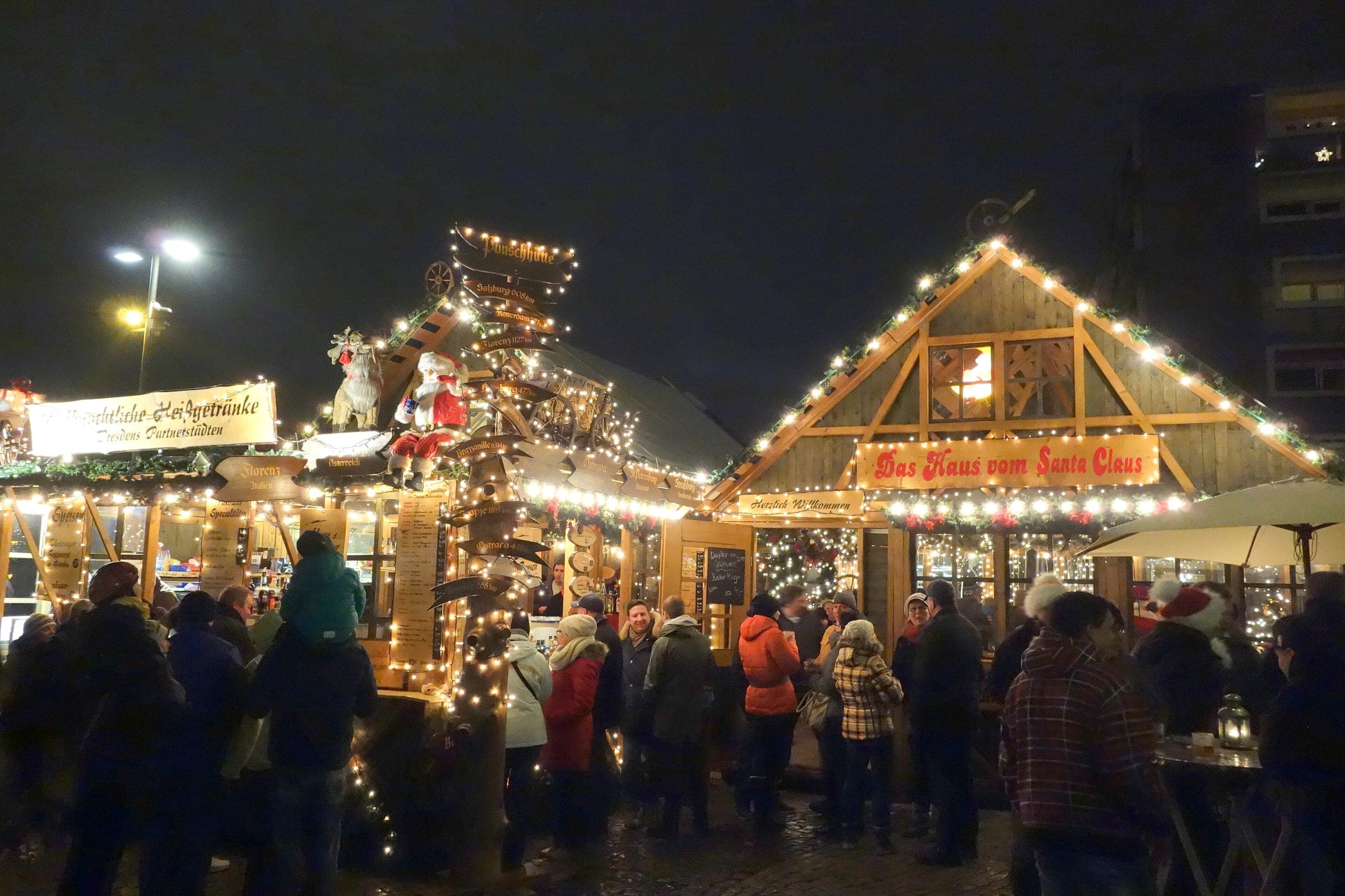 Crowds gather at lit timber stalls with carved figures on the roofs at the Augustusmarkt in Dresden.
