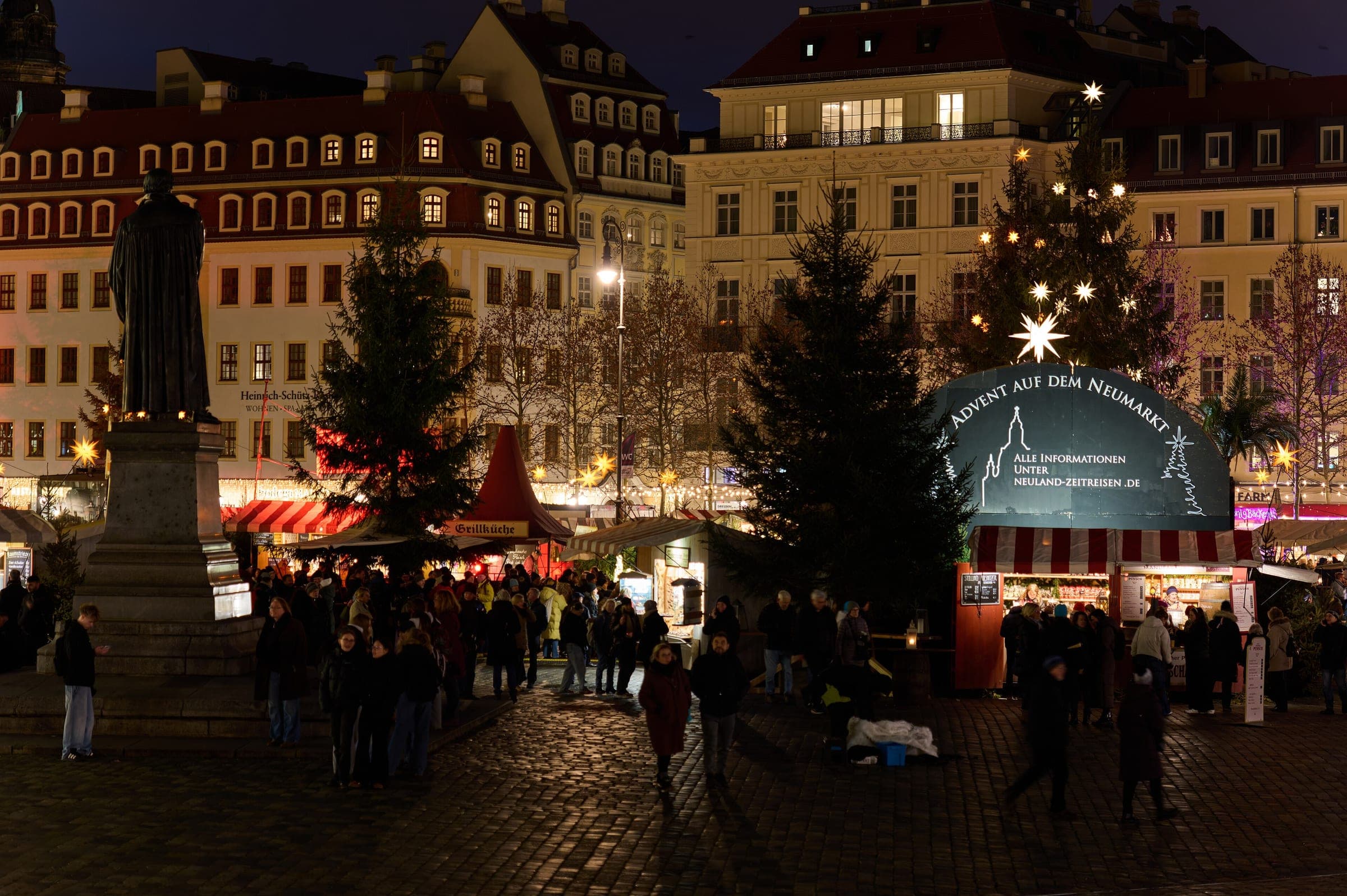 The Luther statue stands among Christmas trees and lit stalls at Advent on the Neumarkt in Dresden.