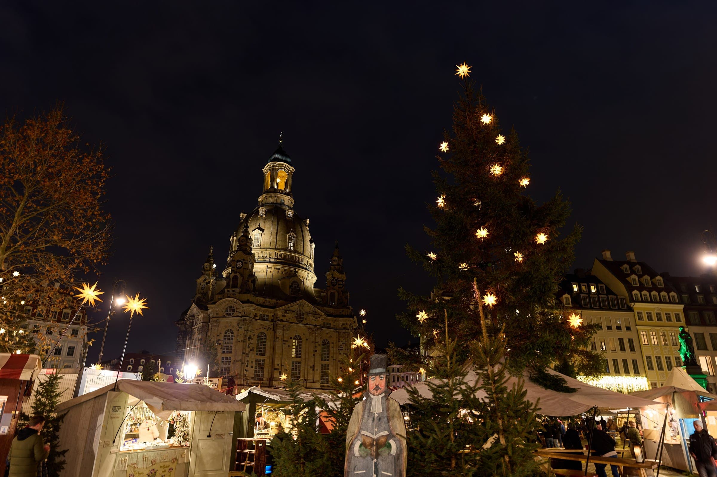 The Frauenkirche dome rises over lit stalls and a starred Christmas tree on Dresden's Neumarkt at night.