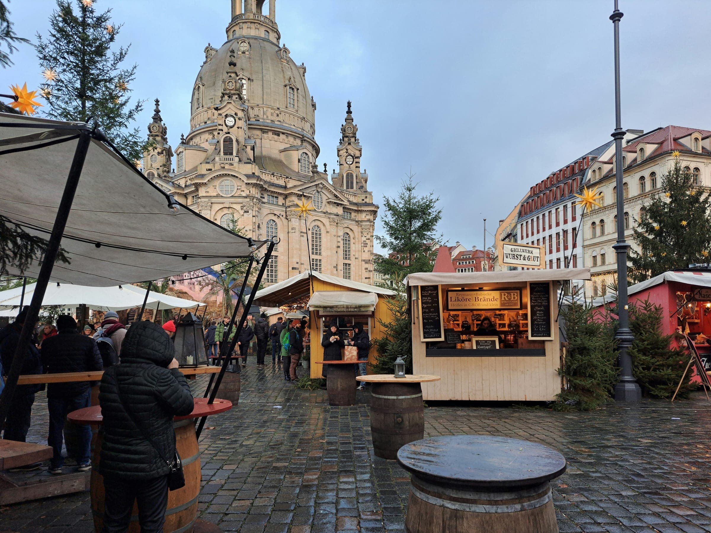 Market stalls and fir trees fill the Neumarkt in front of the sandstone Frauenkirche on a clear December day.
