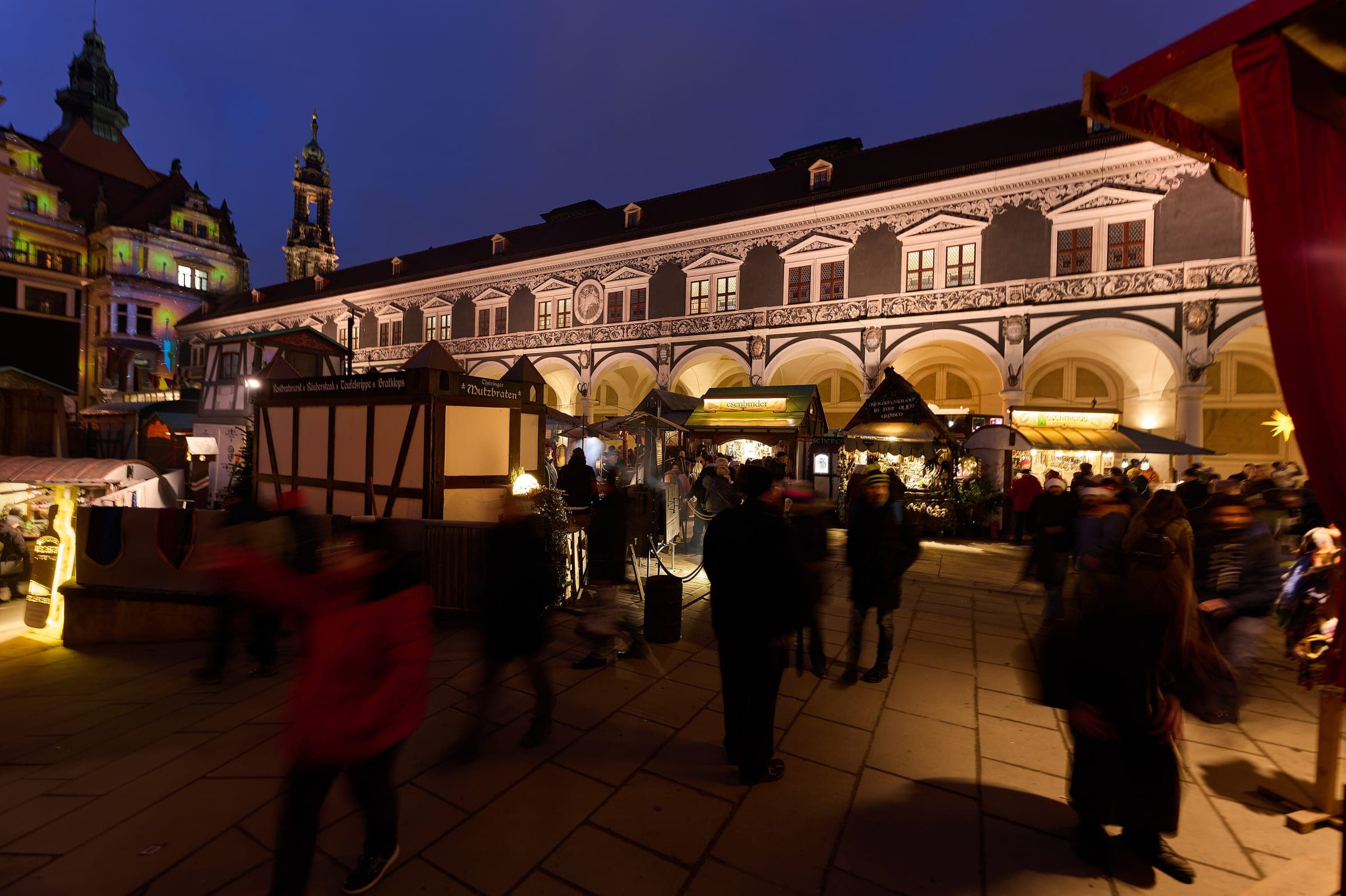Lit timber stalls line the Renaissance arcades of the Stallhof in Dresden at blue hour.