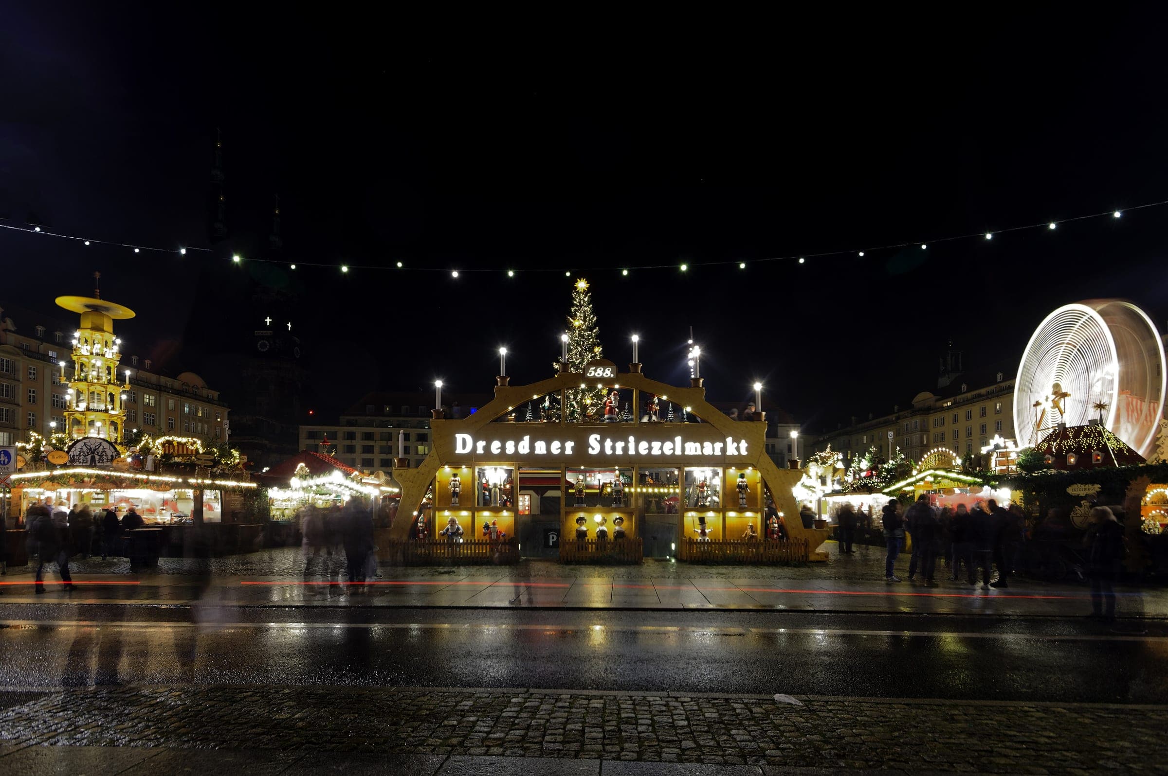The Striezelmarkt fills Dresden's Altmarkt at night with its pyramid, candle arch, tree and Ferris wheel lit.