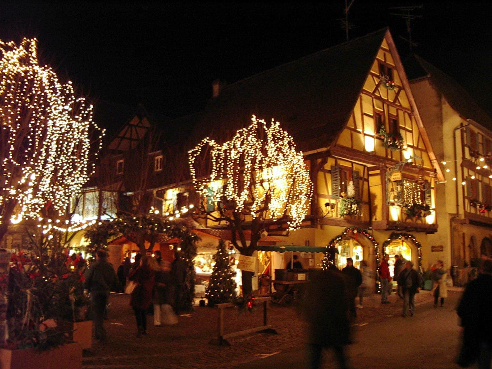 Lit trees and glowing half-timbered houses frame the Christmas market in Eguisheim at night.