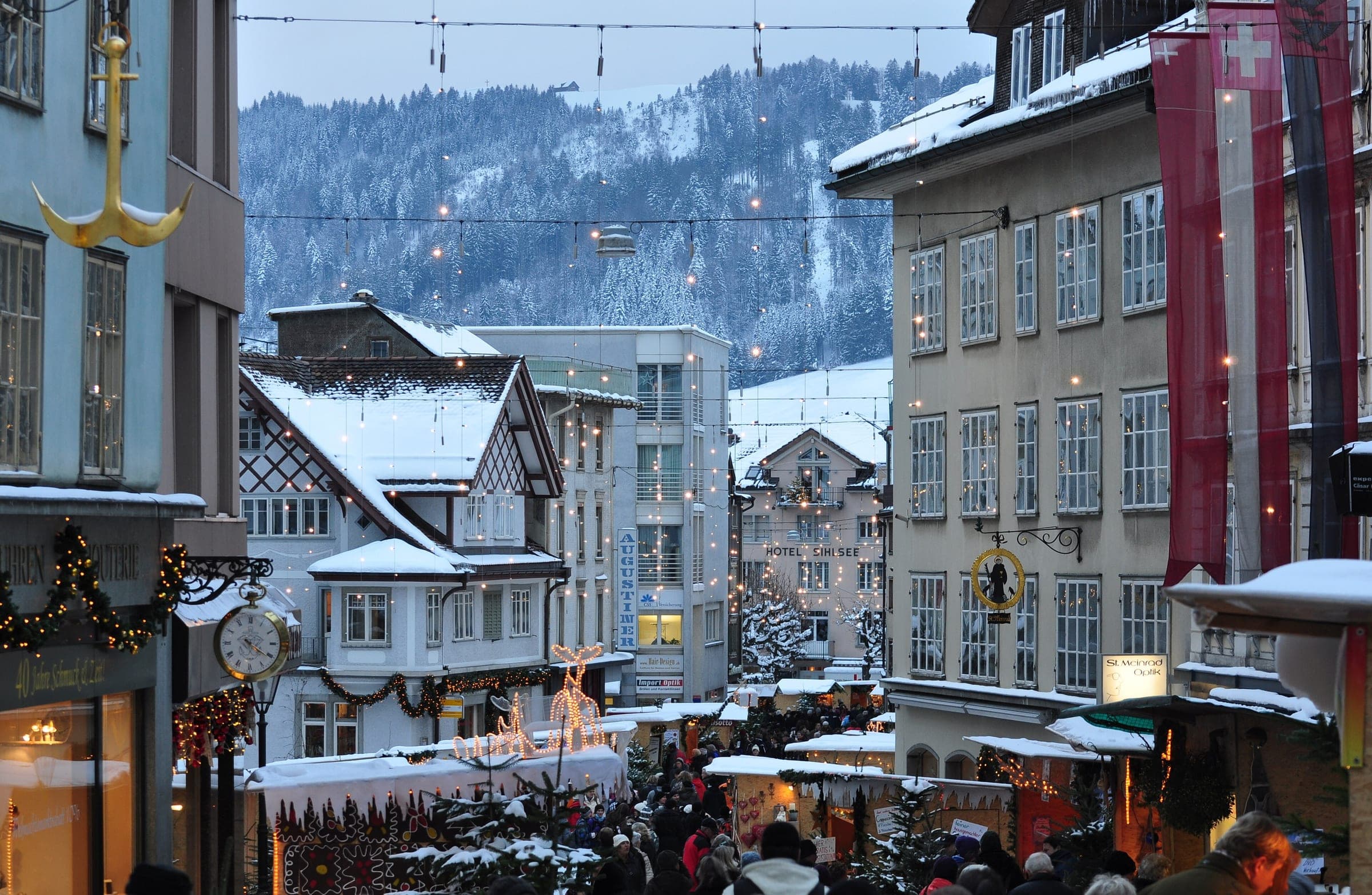 Christmas market stalls line the snowy Hauptstrasse in Einsiedeln under garlands and wooded hills