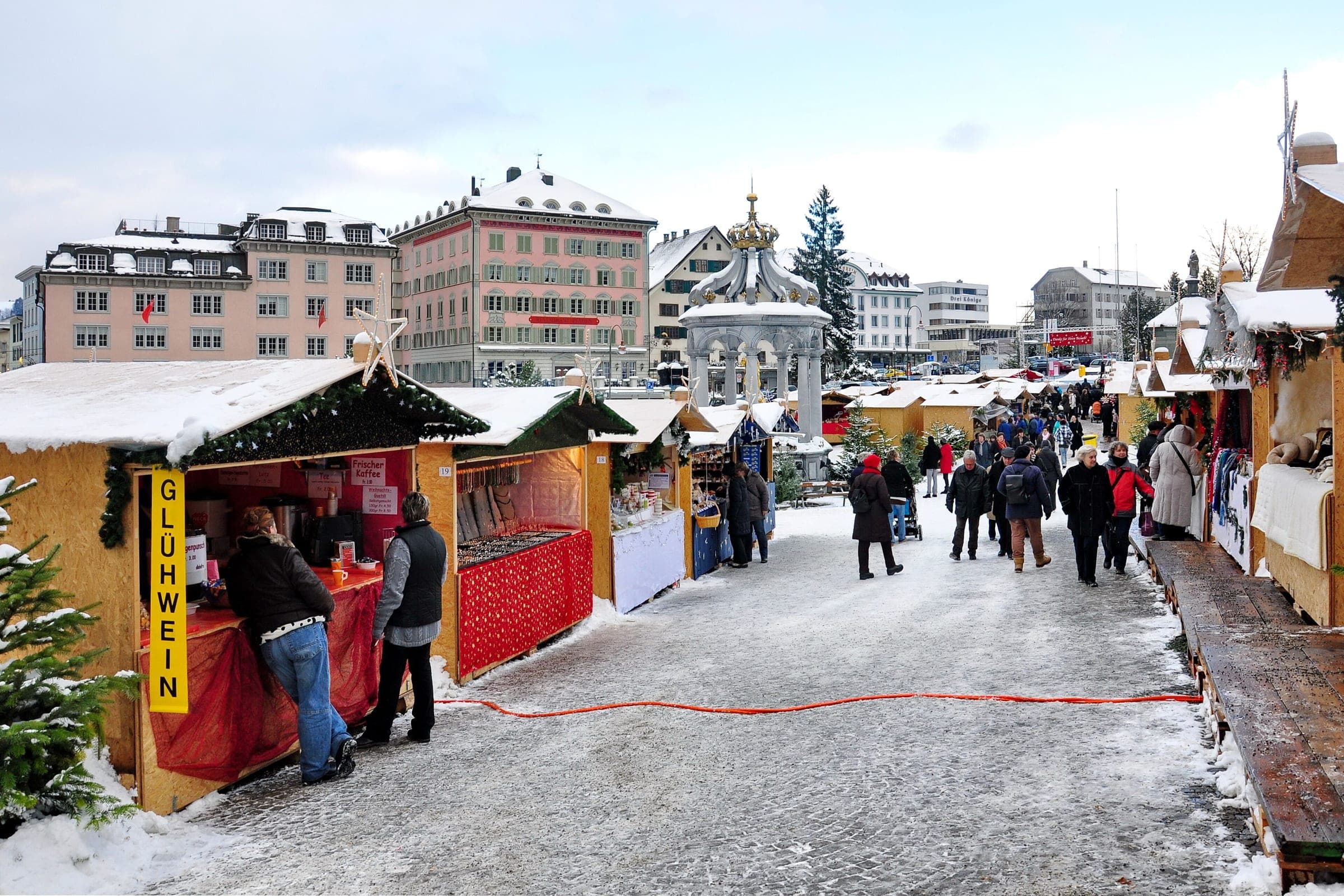 A mulled wine stall opens onto a snowy lane of market huts on the square in Einsiedeln