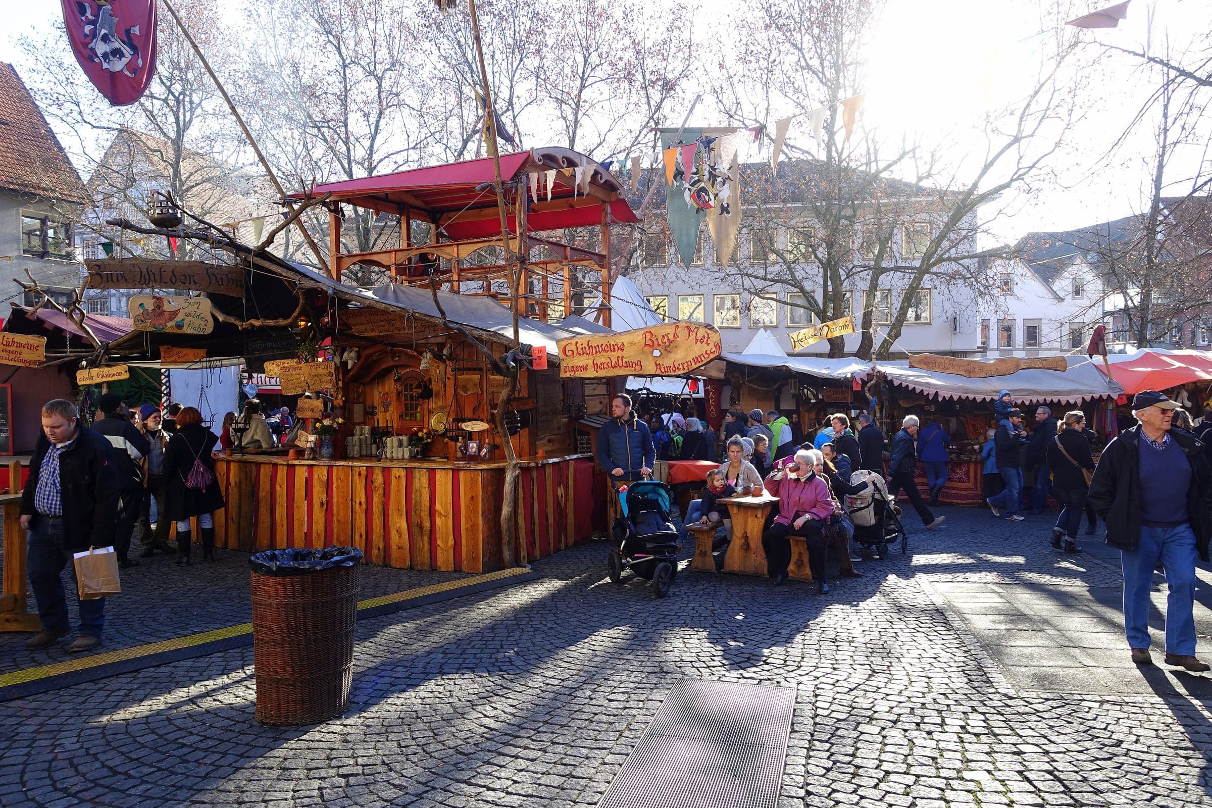 Visitors stroll past timber stalls and red canopies at the Esslingen medieval market on a sunny December day.
