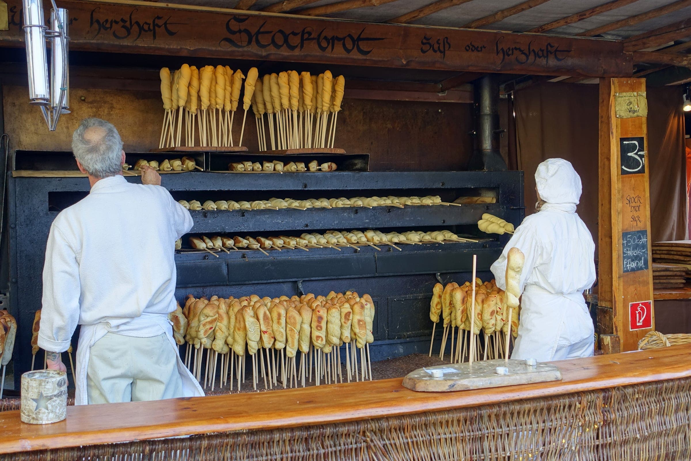 Bakers in white turn Stockbrot over the coals at a wooden stall at the Esslingen medieval market.
