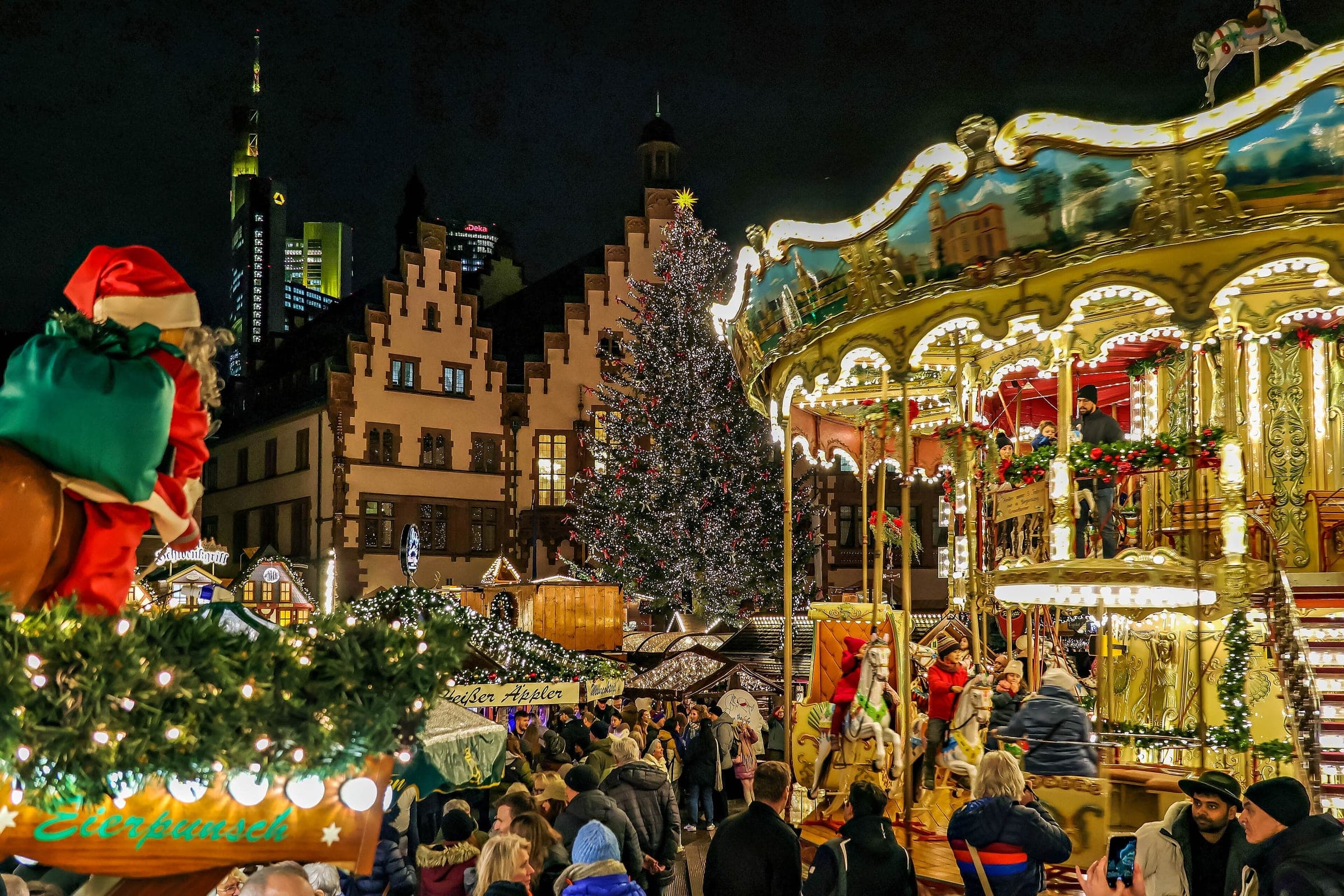 A two-storey carousel spins beside the Christmas tree on Frankfurt's Römerberg as crowds pass at night.
