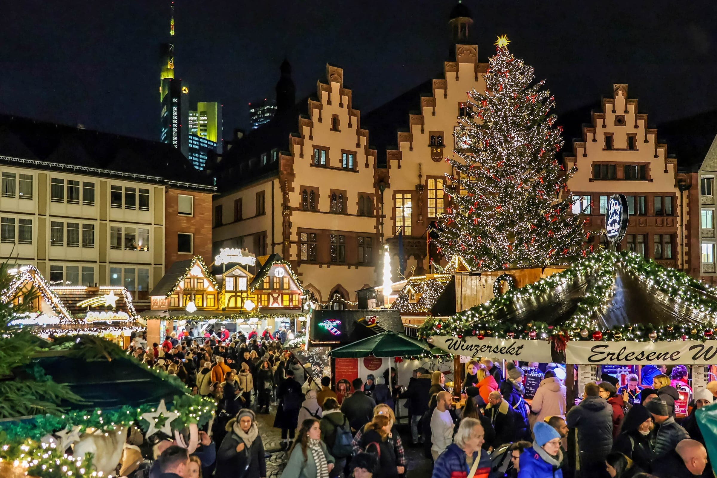 Crowds fill the Römerberg in Frankfurt at night below the stepped gables of the Römer and the Christmas tree.