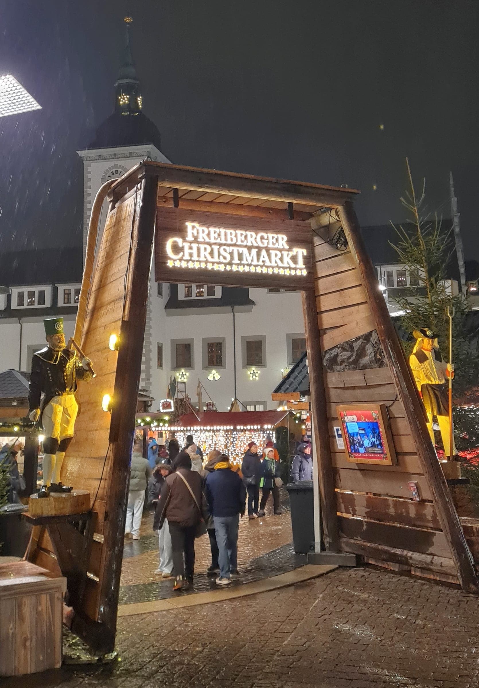 Visitors walk through the timber mine-portal entrance of the Freiberger Christmarkt on a wet night.
