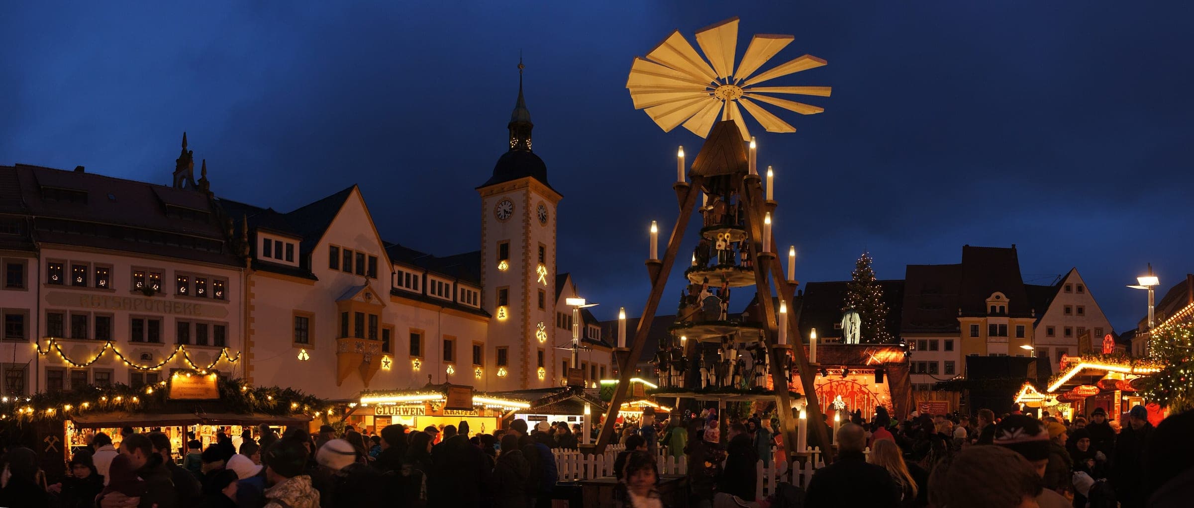 The candlelit pyramid and lit stalls fill Freiberg's Obermarkt in front of the town hall at dusk.