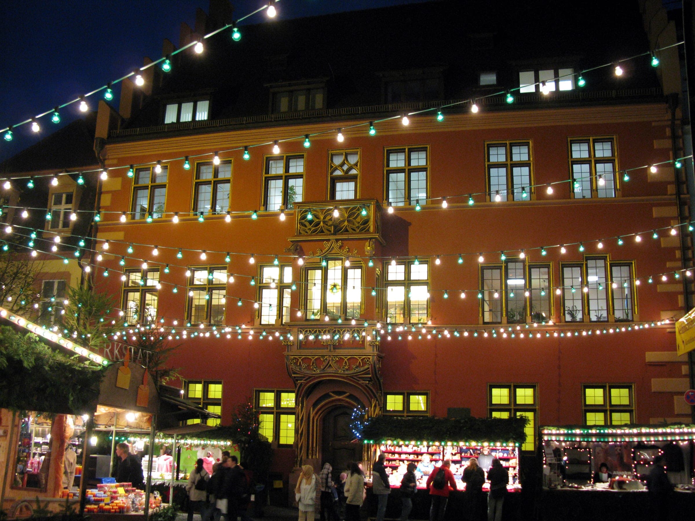 Strings of lights hang across the Rathausplatz in Freiburg in front of the red Altes Rathaus and market stalls.