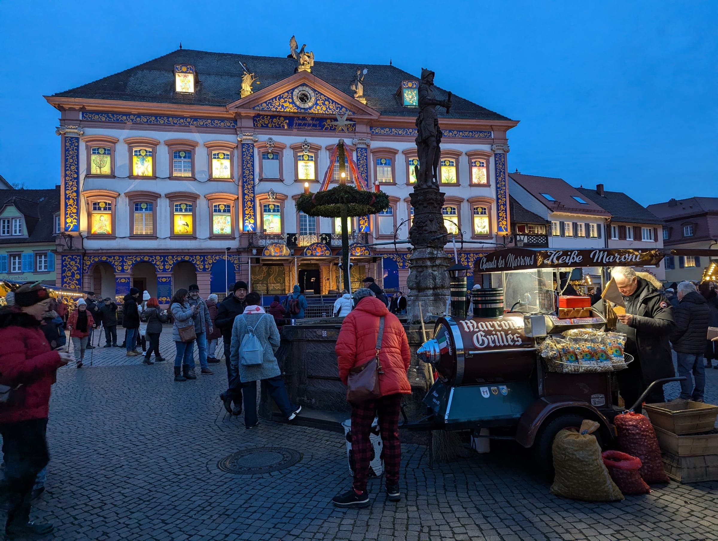 A chestnut roaster's cart stands on Gengenbach's Marktplatz at blue hour below the lit Rathaus windows.