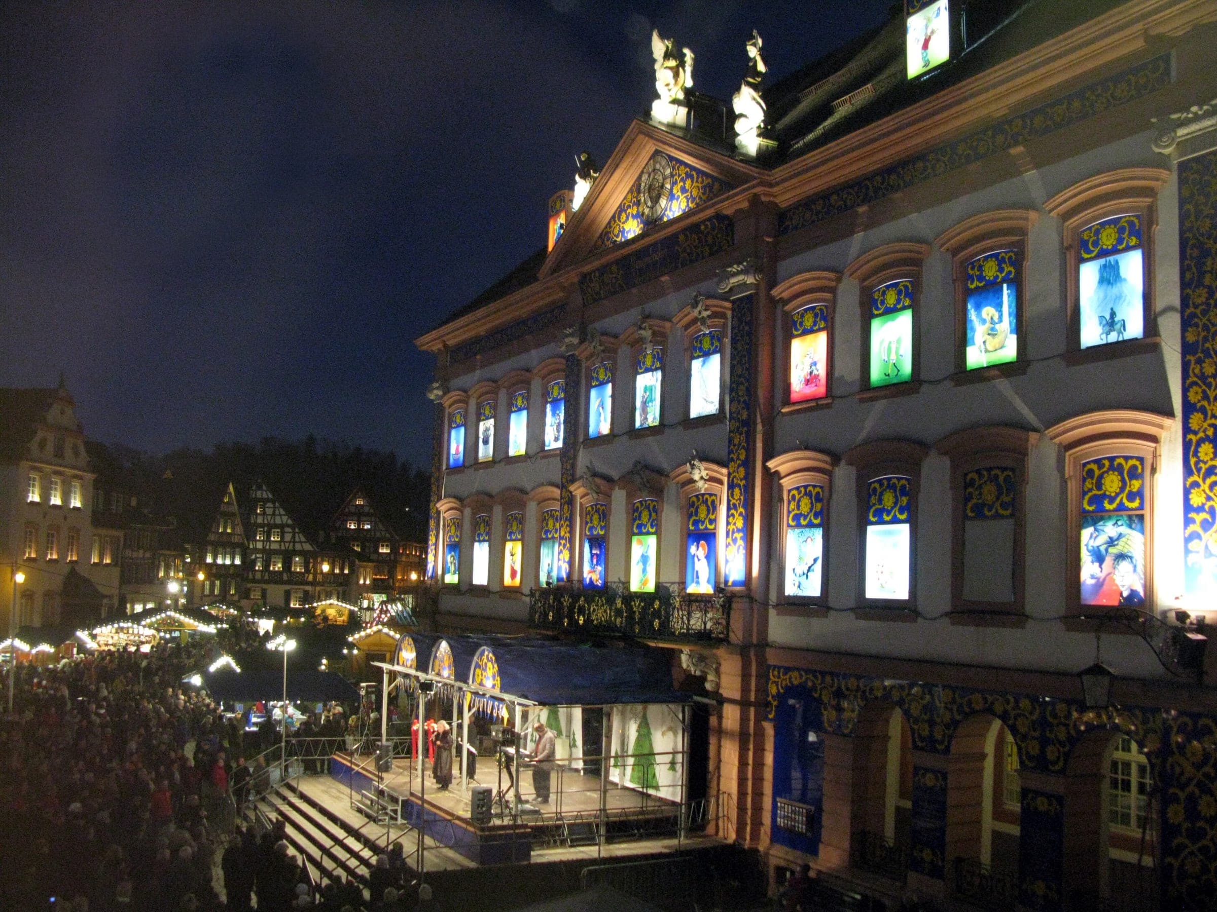 The Rathaus in Gengenbach glows with its Advent calendar windows as a crowd gathers by the stage at night.
