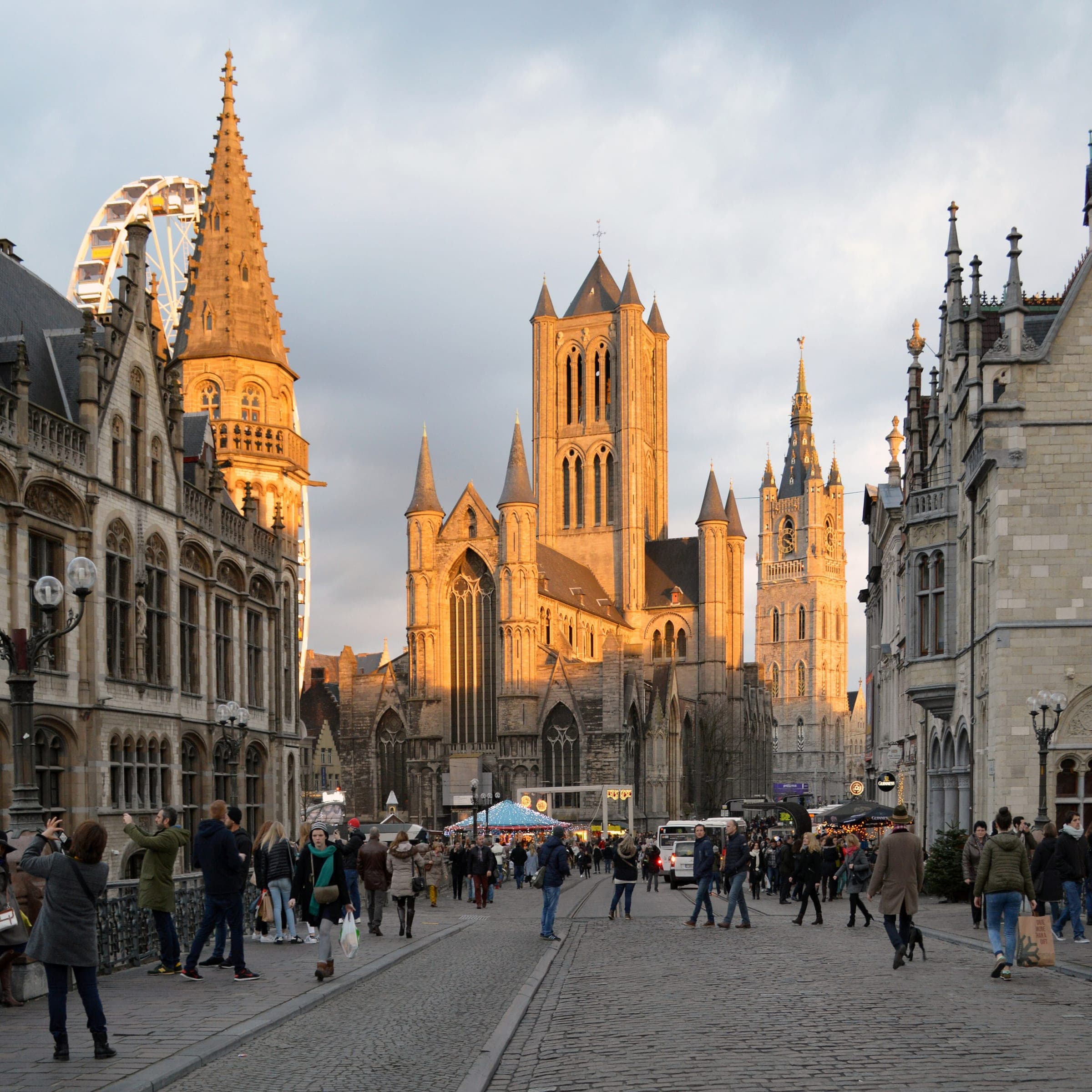 Late sun lights St Nicholas' Church and the Belfry as crowds fill the Korenmarkt in Ghent below the Ferris wheel.